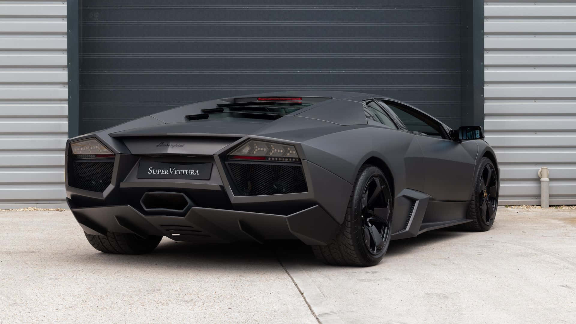 Lamborghini Reventón 桌布 壁紙 — 一輛消光黑色的藍寶堅尼 Reventón SuperVettura 停在工業車庫門前，地面是混凝土。