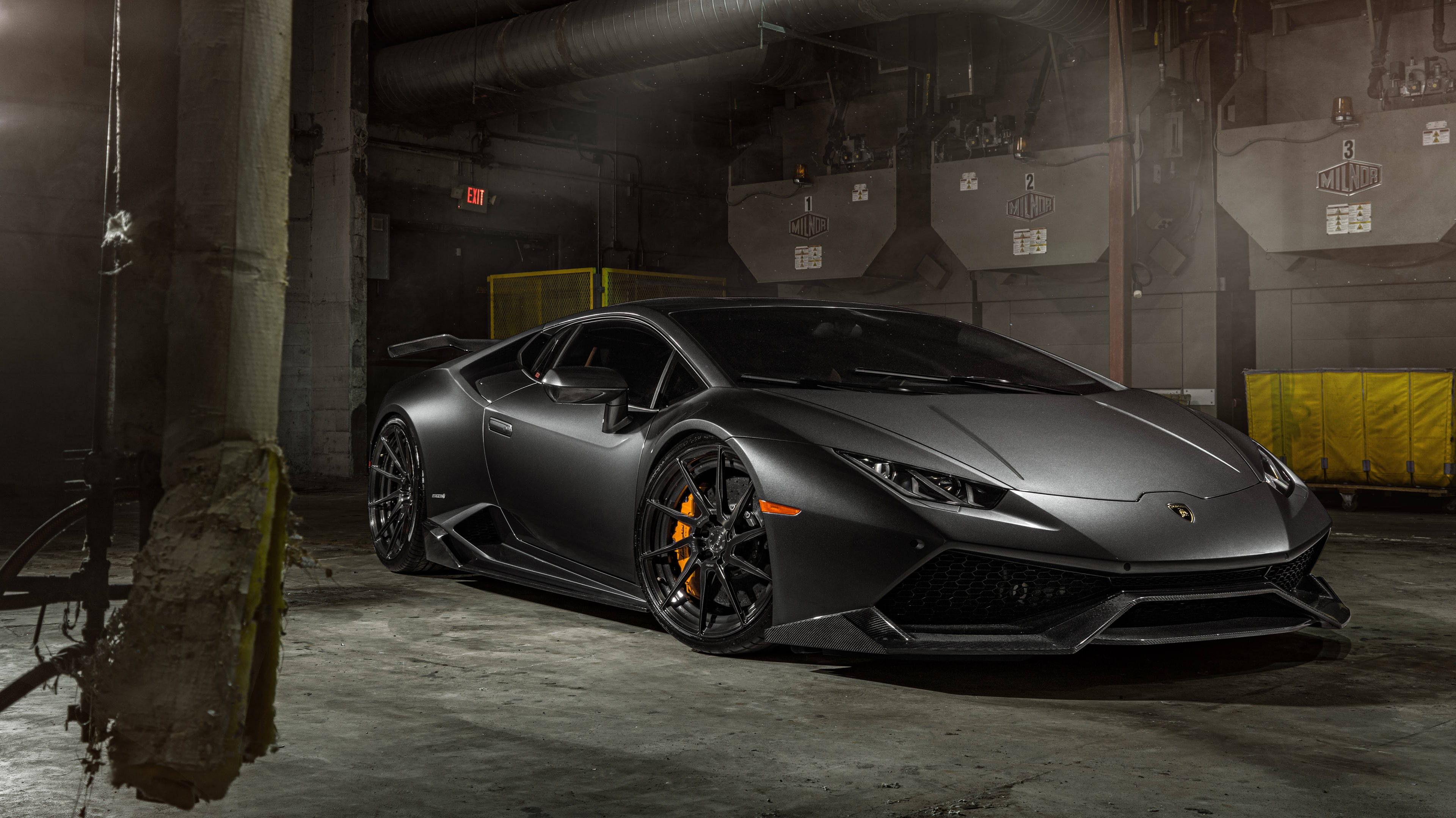 Lamborghini 4K 桌布 壁紙 — 一輛消光黑色的藍寶堅尼Huracán跑車在昏暗的工業車庫中，在戲劇性的燈光下閃閃發光。
