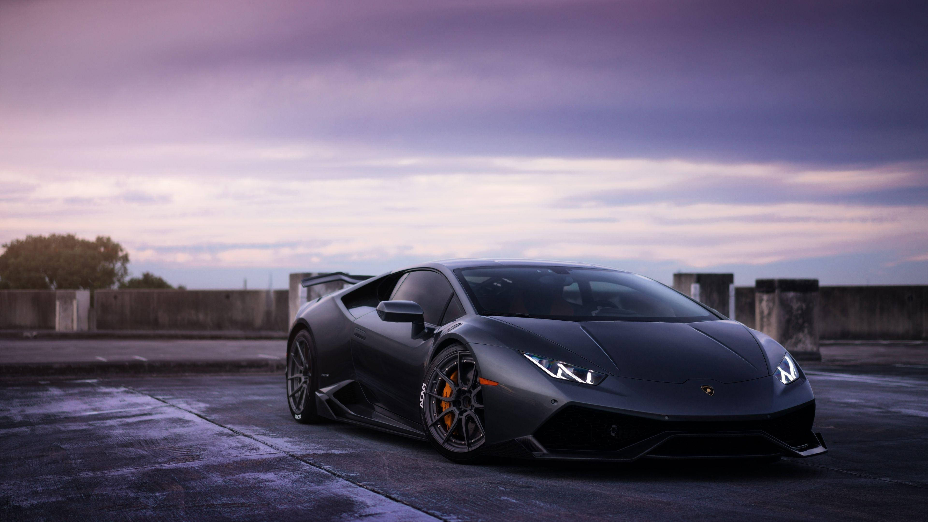Lamborghini 4K 桌布 壁紙 — 一輛消光黑色的藍寶堅尼Huracán跑車停放在屋頂上，黃昏時分，上方有紫色雲彩。