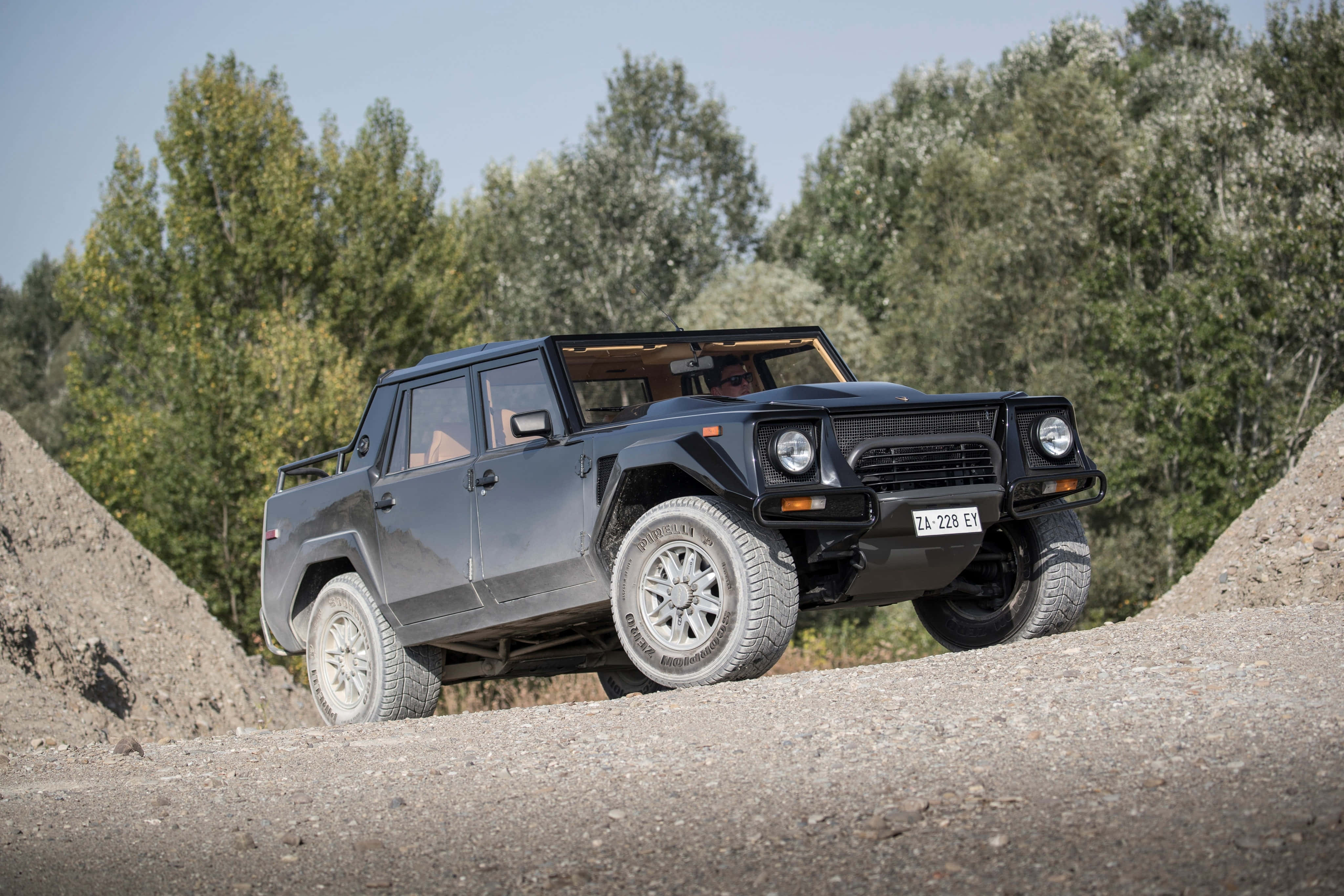 Lamborghini Lm002 桌布 壁紙 — 一輛消光黑色的藍寶堅尼LM002 SUV在晴朗的藍天下，以堅固的輪胎和霸氣的姿態征服陡峭的碎石坡。