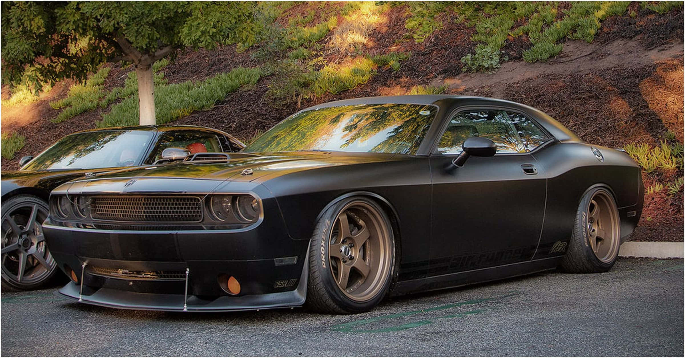 Muscle Cars 桌布 壁紙 — 一輛消光黑色肌肉車搭配青銅輪圈，停在柏油路上，沐浴在金色陽光下，背景有樹木和山丘。