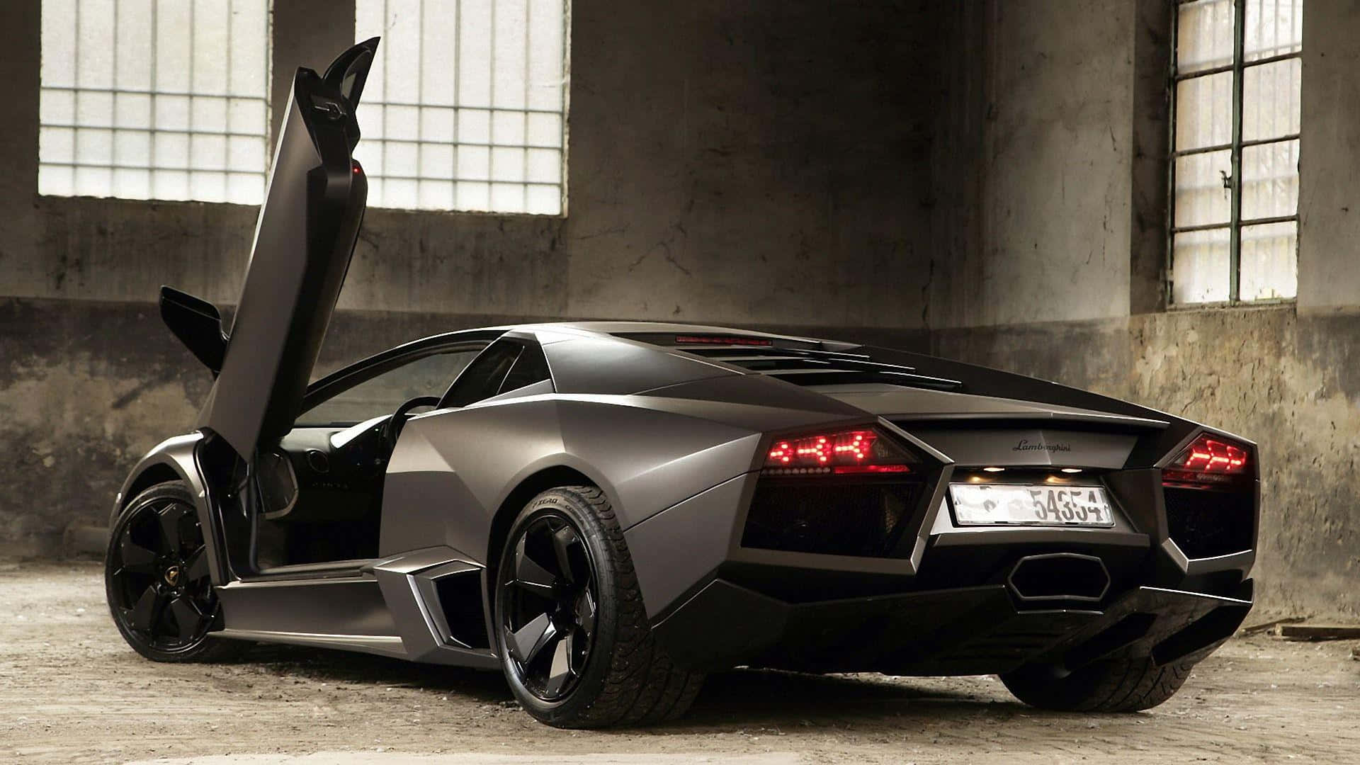 Cool Car 桌布 壁紙 — 一輛消光黑色藍寶堅尼Reventon，鷗翼車門開啟，停在粗獷的工業倉庫中，光線柔和。