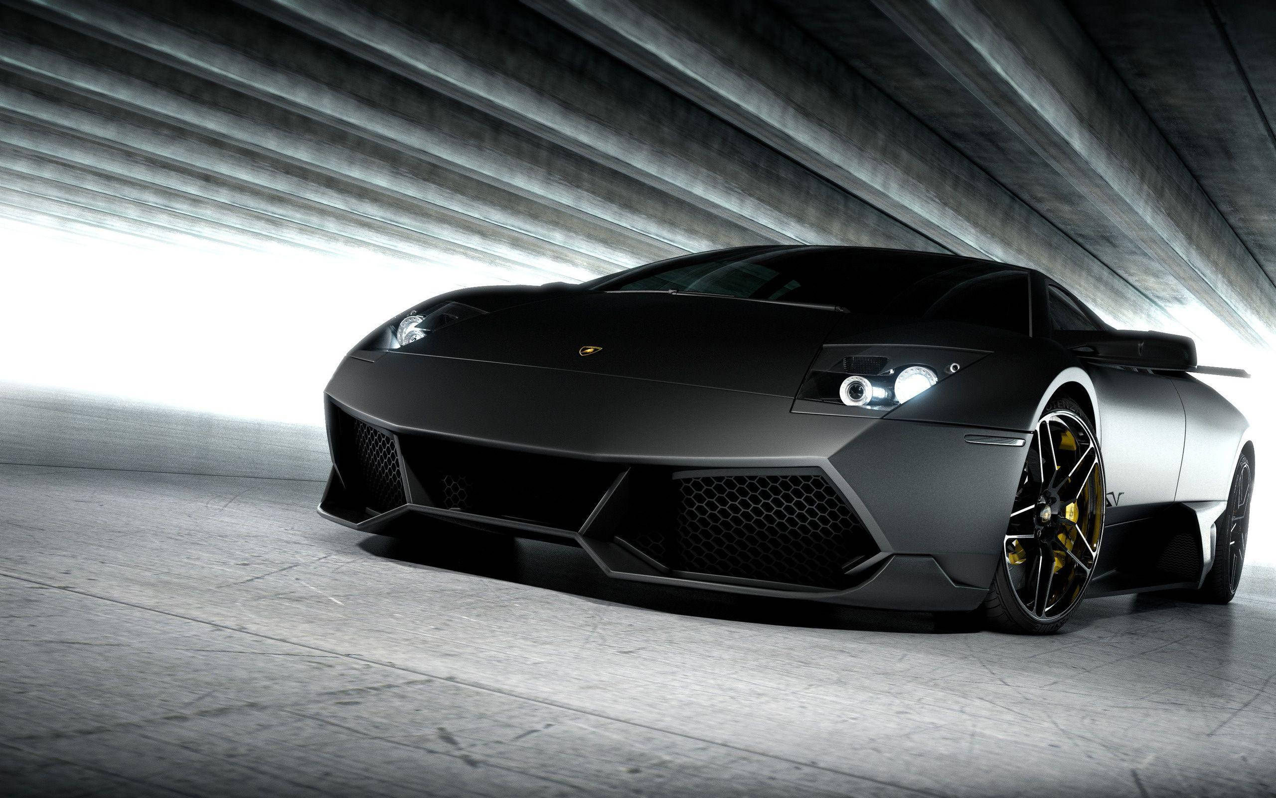 Lamborghini 4K 桌布 壁紙 — 一輛消光黑色藍寶堅尼跑車搭配金色飾邊，在混凝土隧道內的戲劇性燈光下閃閃發光。