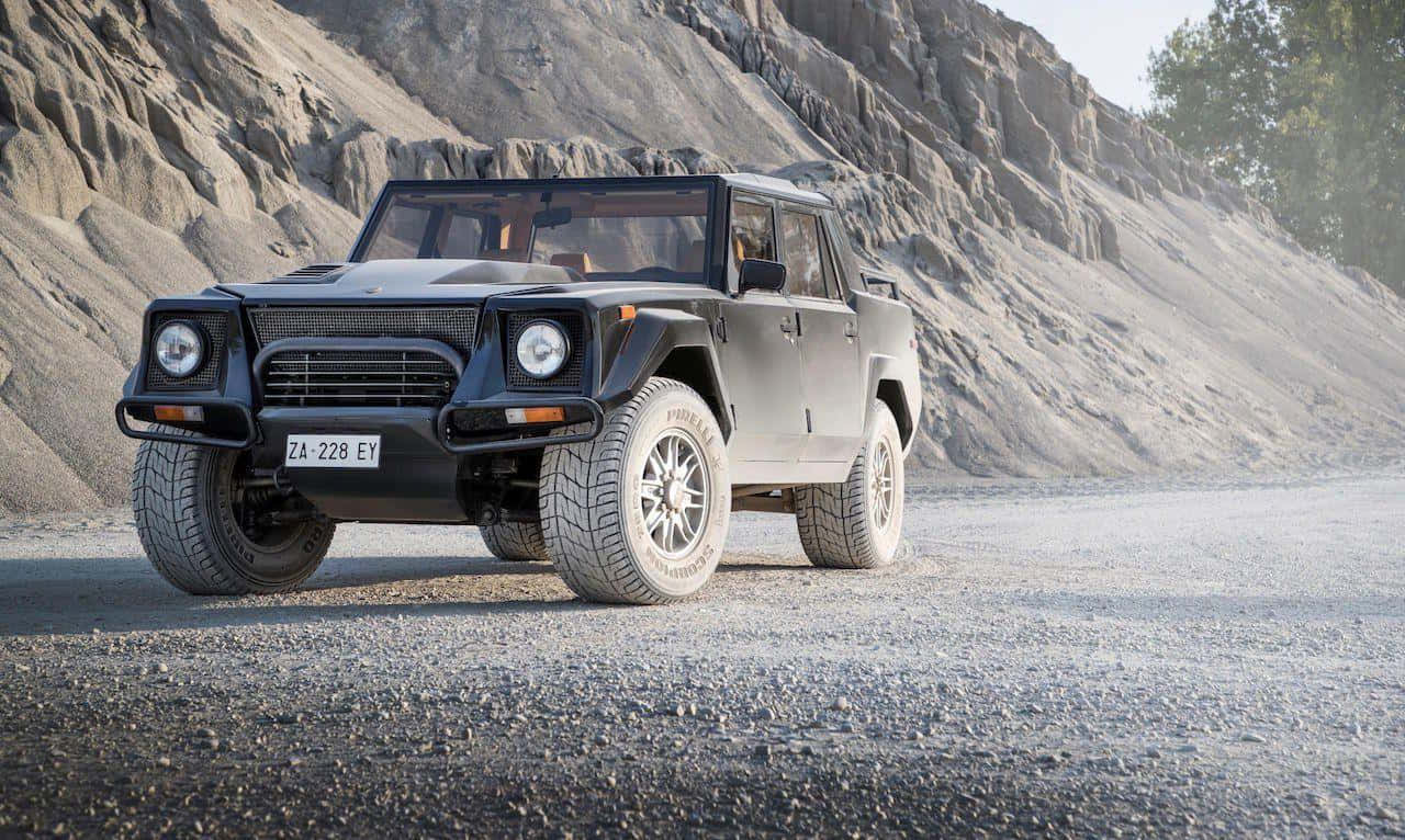 Lamborghini Lm002 桌布 壁紙 — 一輛消光黑色裝甲SUV配備大型輪胎，在明亮的日光下停在碎石路上，背景是崎嶇的岩石懸崖。