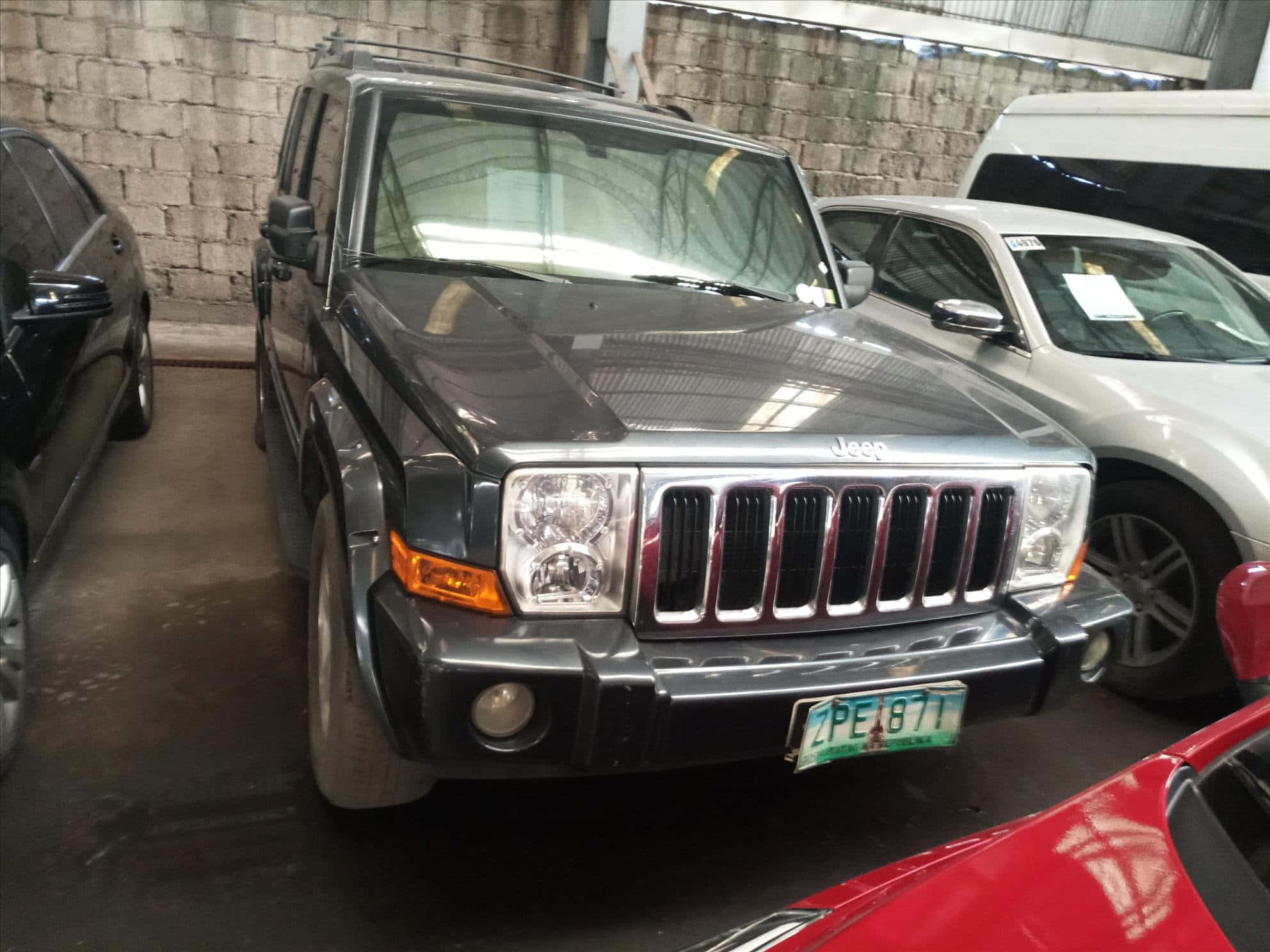 Jeep Commander 桌布 壁紙 — 一輛深灰色Jeep Wrangler停放在室內，背景是混凝土塊牆，周圍有其他車輛。