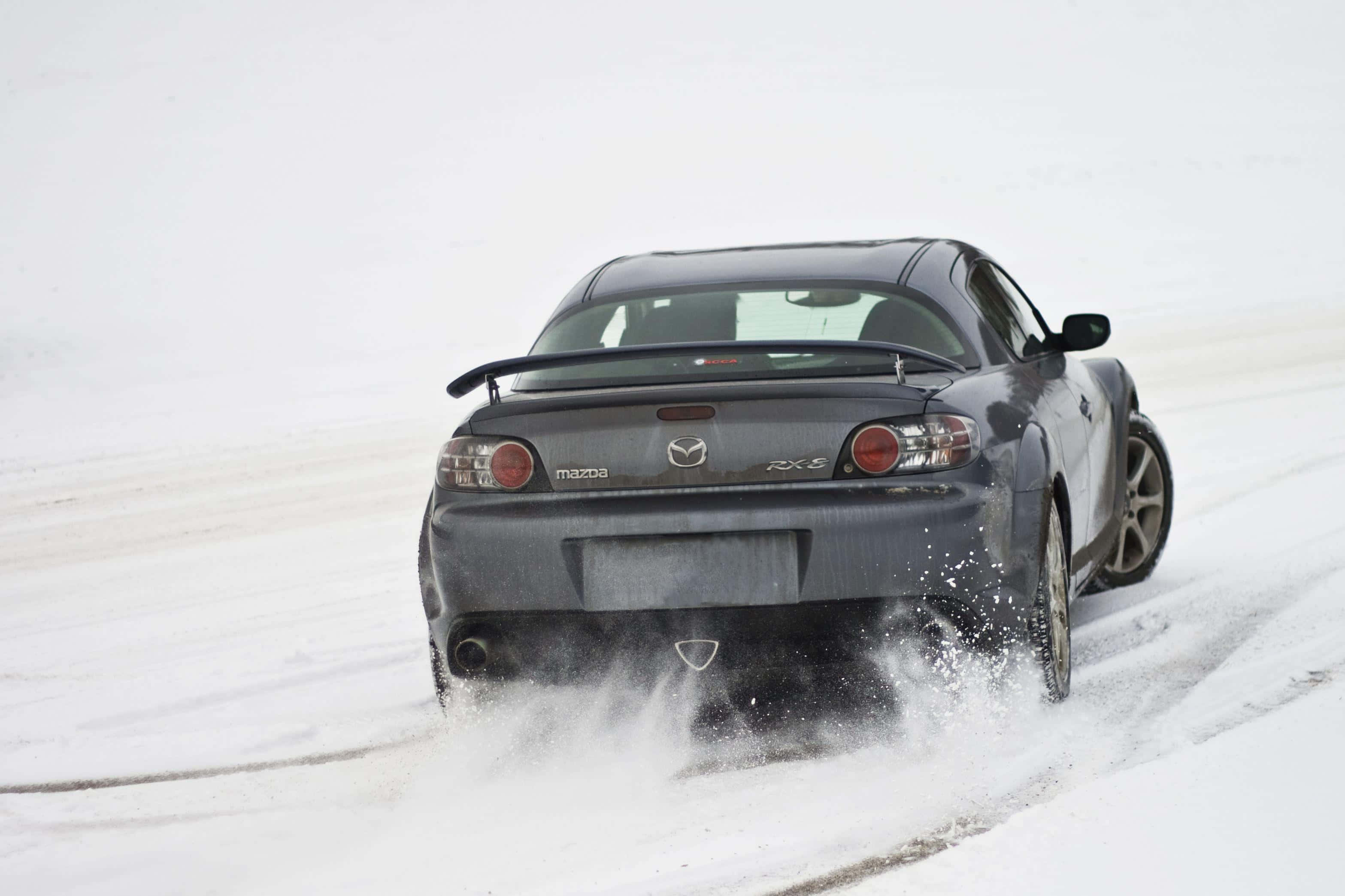 Mazda Rx-8 桌布 壁紙 — 一輛深灰色馬自達RX-8跑車在雪景中行駛時揚起雪花。