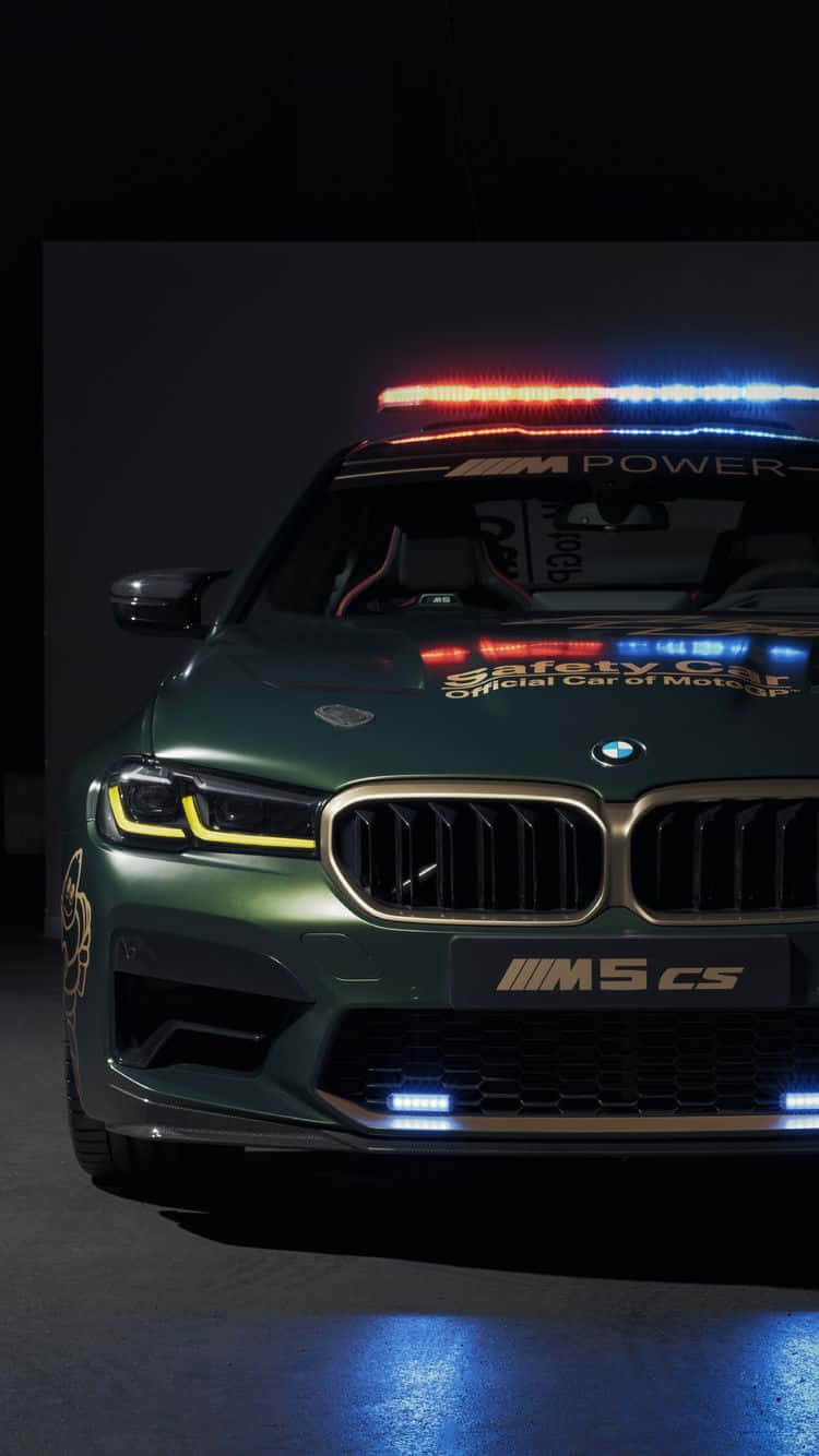 iPhone 桌布 壁紙 — 一輛深綠色BMW M5 CS安全車，閃爍著紅色和藍色的燈光，主導著昏暗的攝影棚環境。