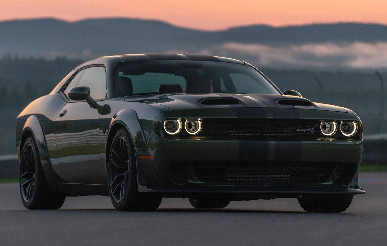 Challenger 桌布 壁紙 — 一輛深綠色Dodge Challenger SRT Hellcat帶有黑色賽車條紋，停在日落時分的道路上，背景是山脈。