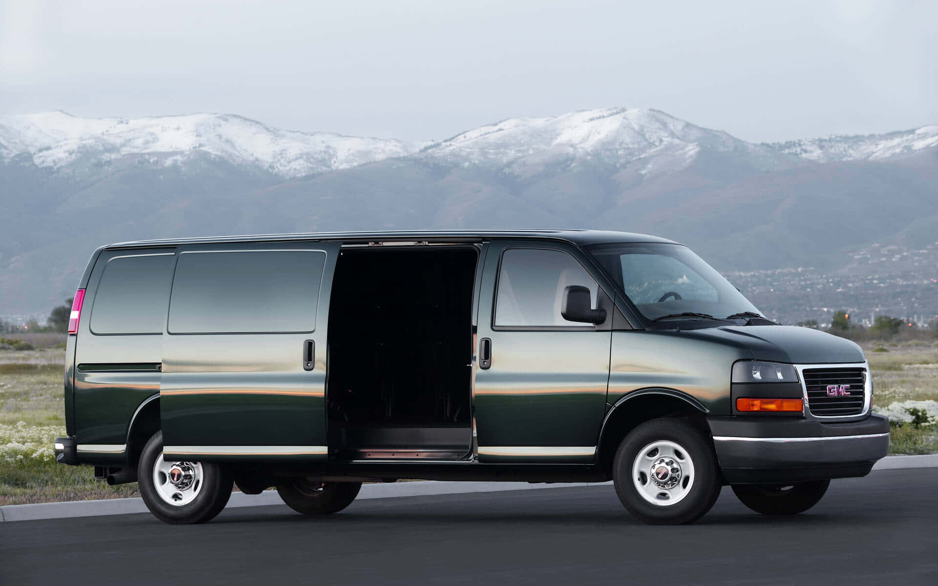 Gmc Savana 桌布 壁紙 — 一輛深綠色GMC廂型車側門打開，停在路上，背景是白雪覆蓋的山脈。