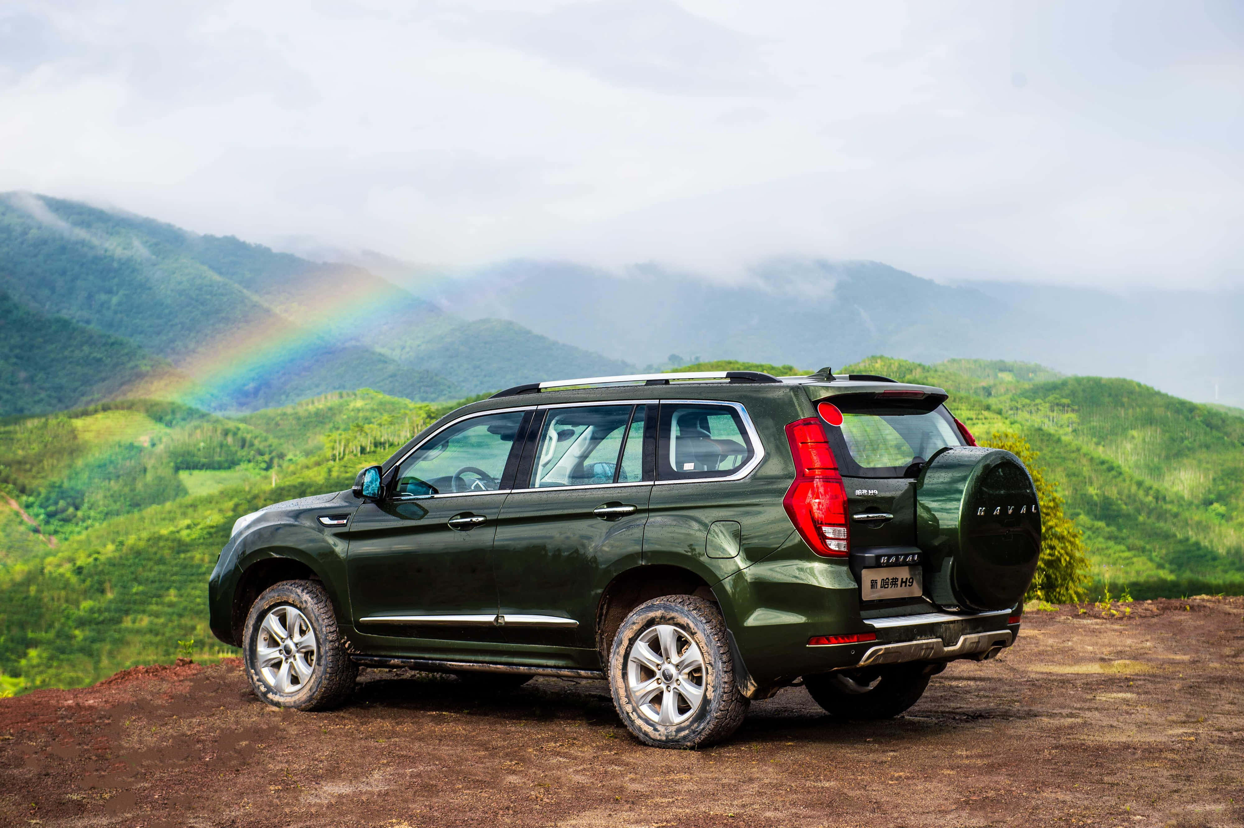 Haval 桌布 壁紙 — 一輛深綠色SUV停泊在泥土觀景點，彩虹在雲天下拱起於翠綠山巒之上。