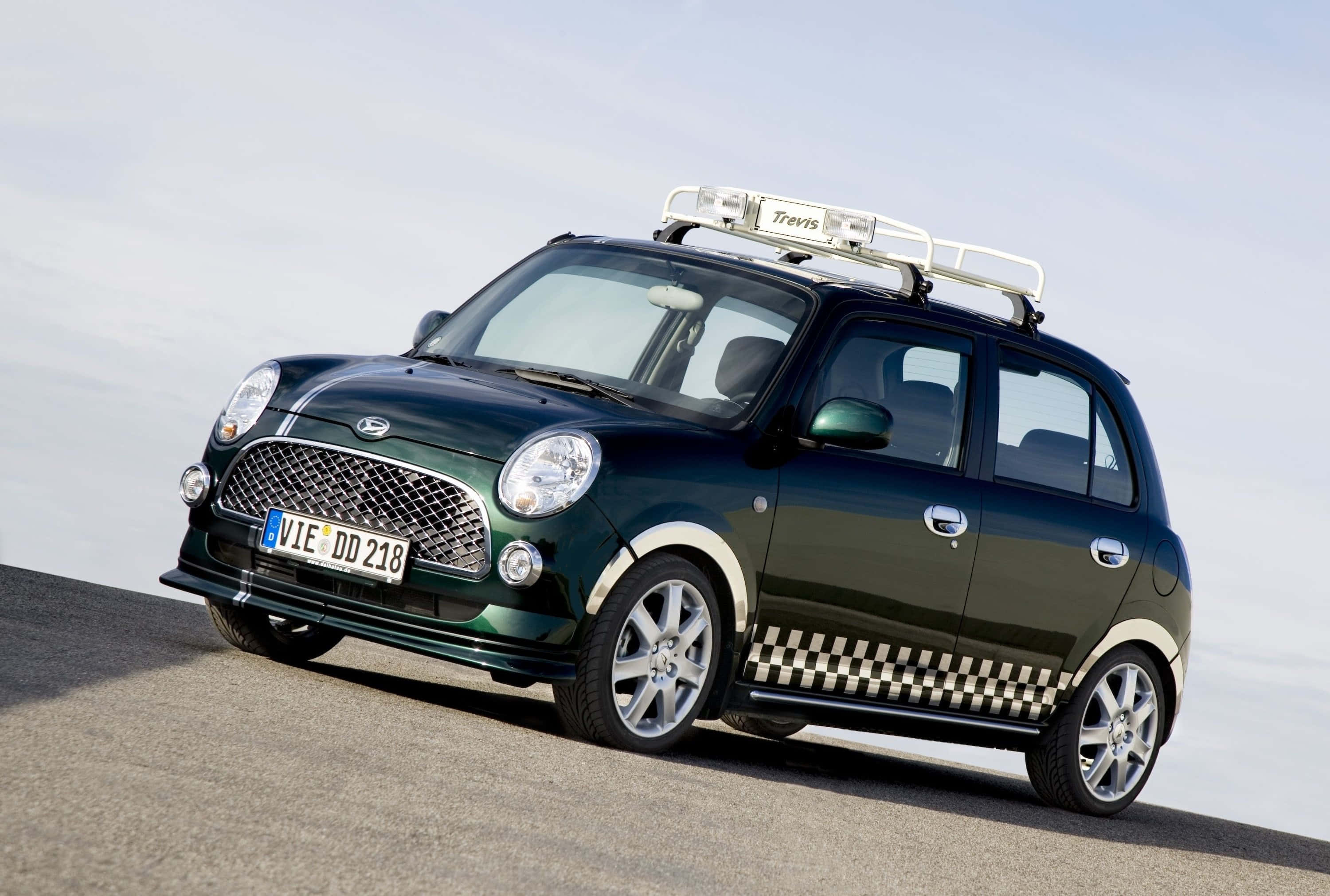 Daihatsu 桌布 壁紙 — 一輛深綠色小型車，帶有格子側條紋和車頂行李架，停在柏油路上，天空蒼白。