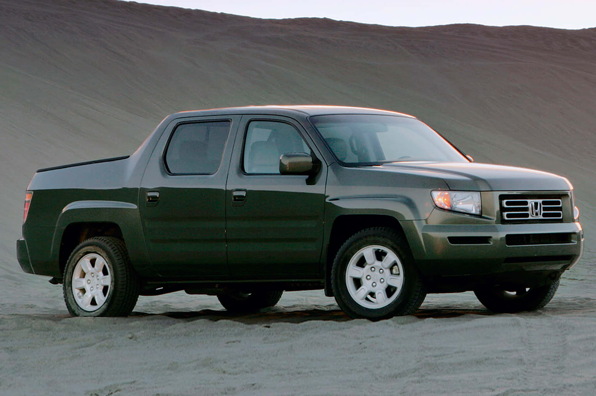 Honda Ridgeline 桌布 壁紙 — 一輛深綠色本田Ridgeline皮卡車停在沙地上，背景有起伏的山丘。