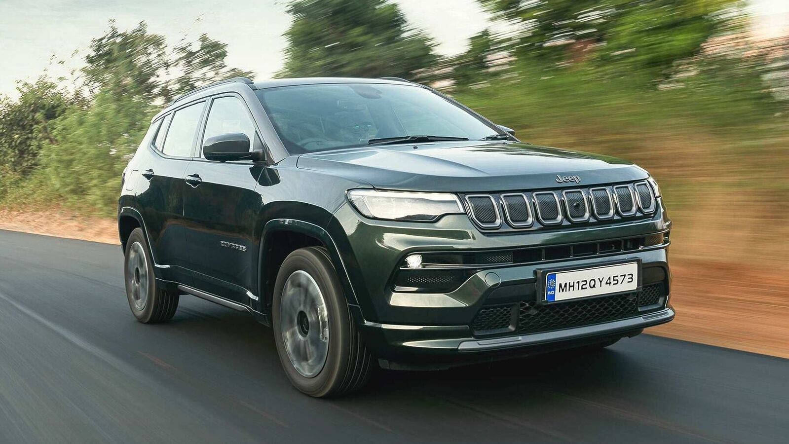 driving 桌布 壁紙 — 一輛深綠色的Jeep Compass SUV在道路上疾馳，背景是模糊的綠色植物。
