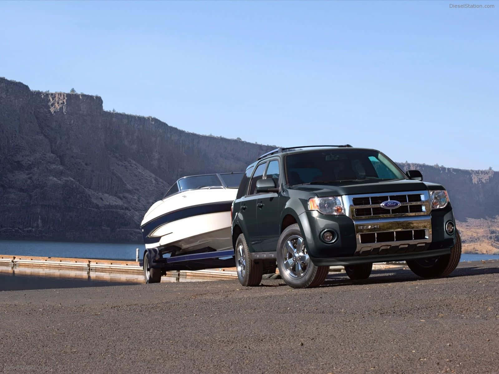 Ford Escape 桌布 壁紙 — 一輛深綠色福特Explorer SUV在晴朗藍天下沿著湖邊道路拖著一艘白色快艇，旁邊有岩石峭壁。