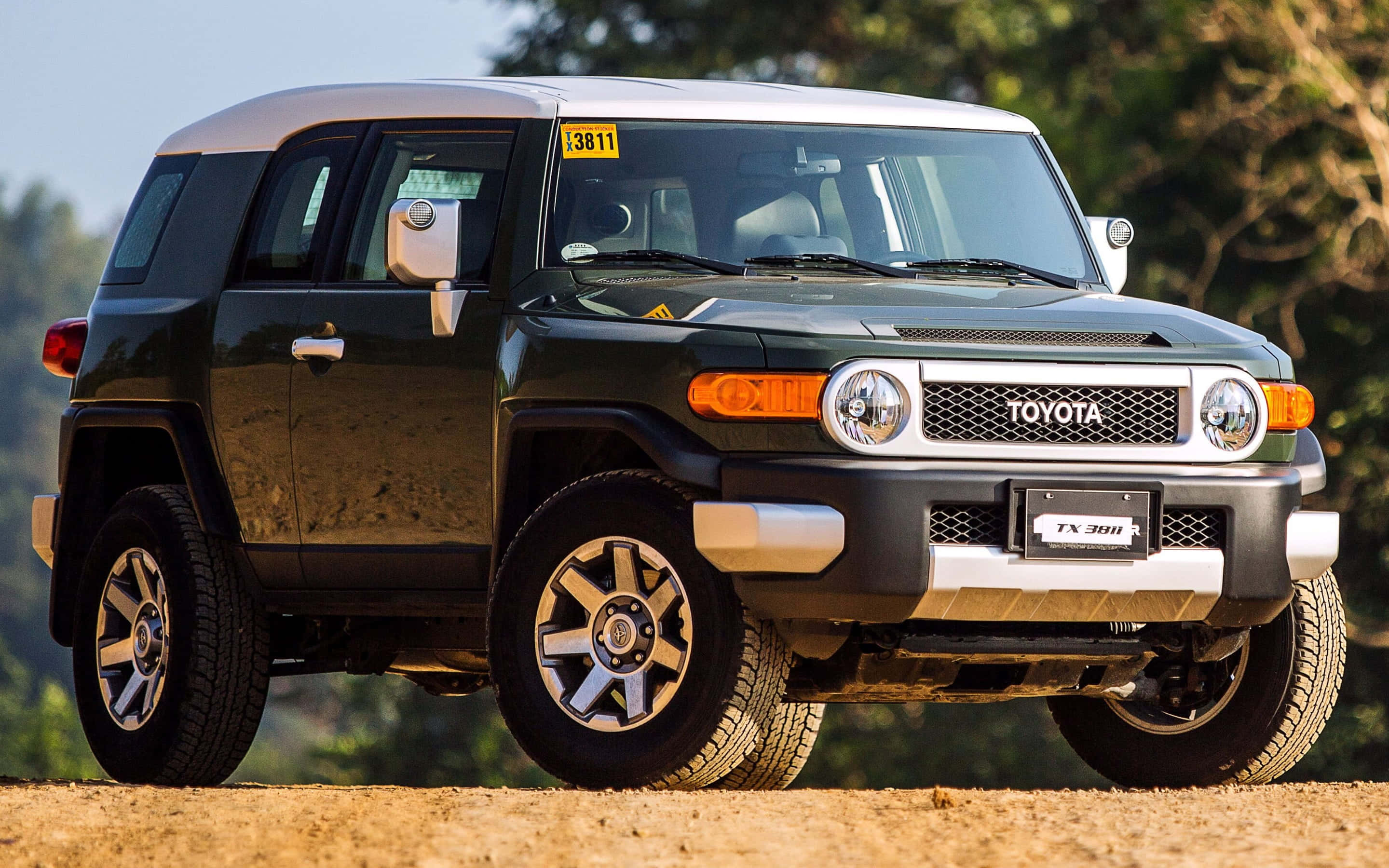豐田 桌布 壁紙 — 一輛深綠色豐田FJ Cruiser SUV停在泥路上，背景有樹木，光線明亮。