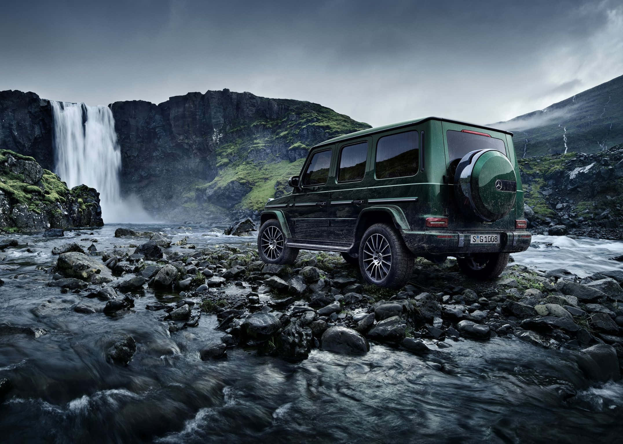 2152x1536 桌布 壁紙 — 一輛深綠色賓士G-Class SUV在暴風雨天空下，堅固地停在岩石地形上，旁邊是層疊瀑布。