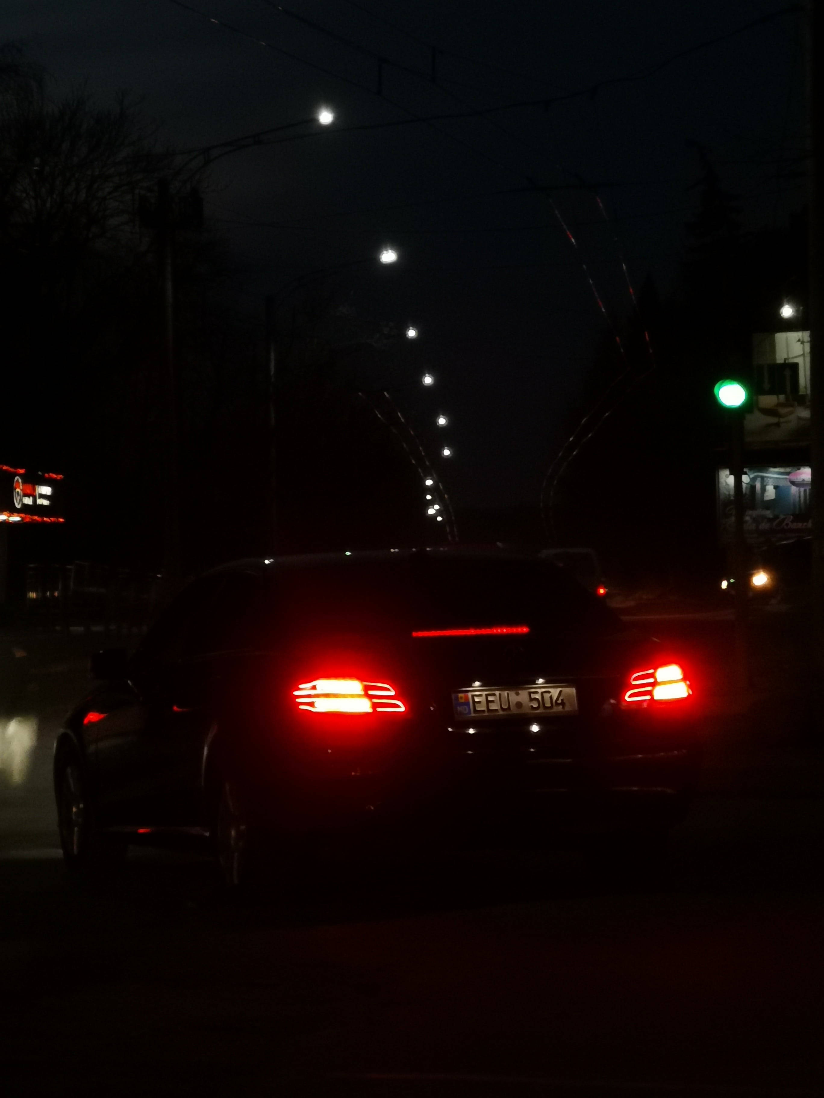 X 桌布 壁紙 — 一輛深色轎車發光的紅色尾燈照亮了雨夜街道，街道上有一排路燈和一個綠色交通號誌。