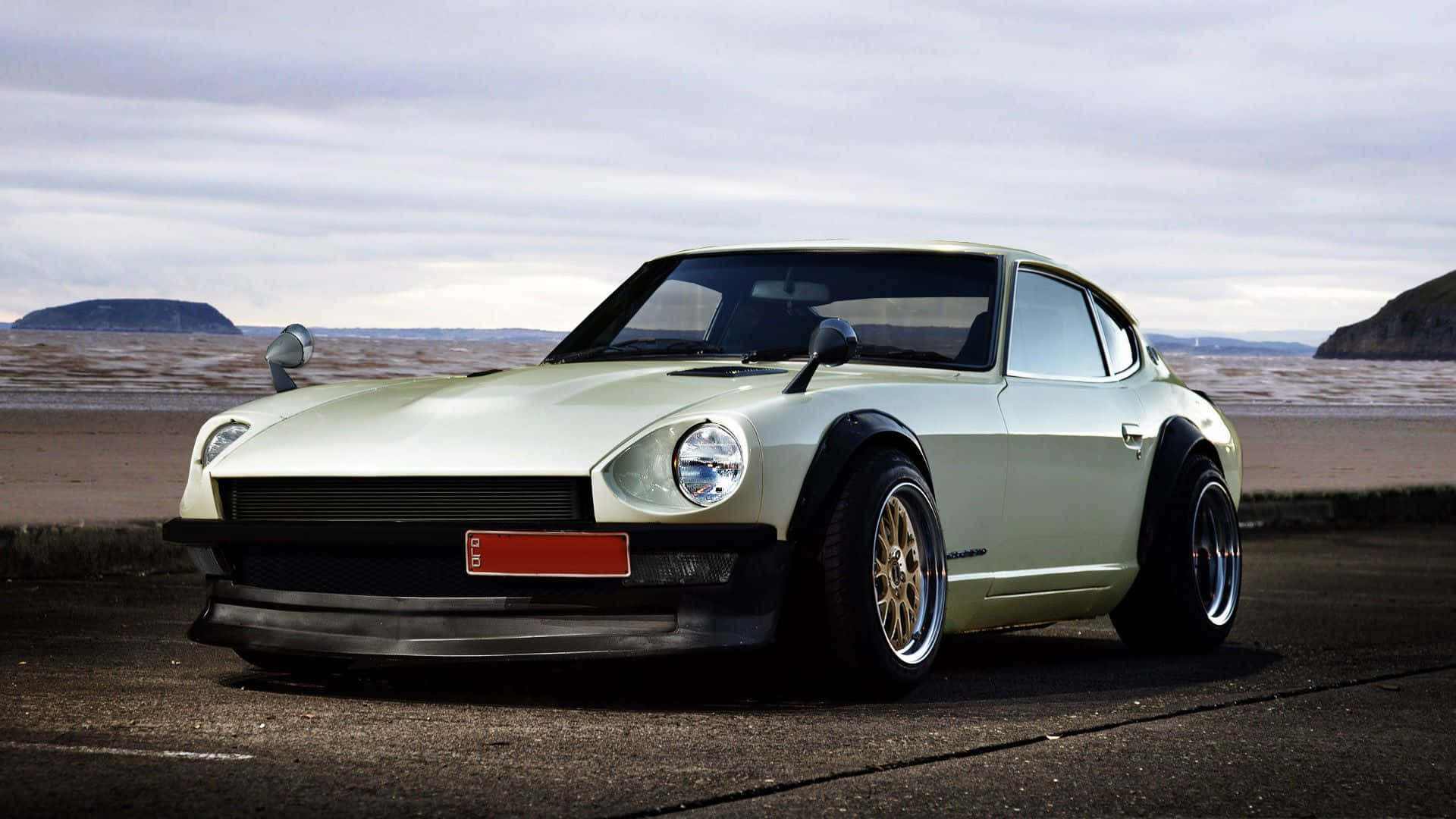 Datsun 桌布 壁紙 — 一輛淺綠色經典跑車配金色輪圈，停泊在陰天下的海岸公路上。