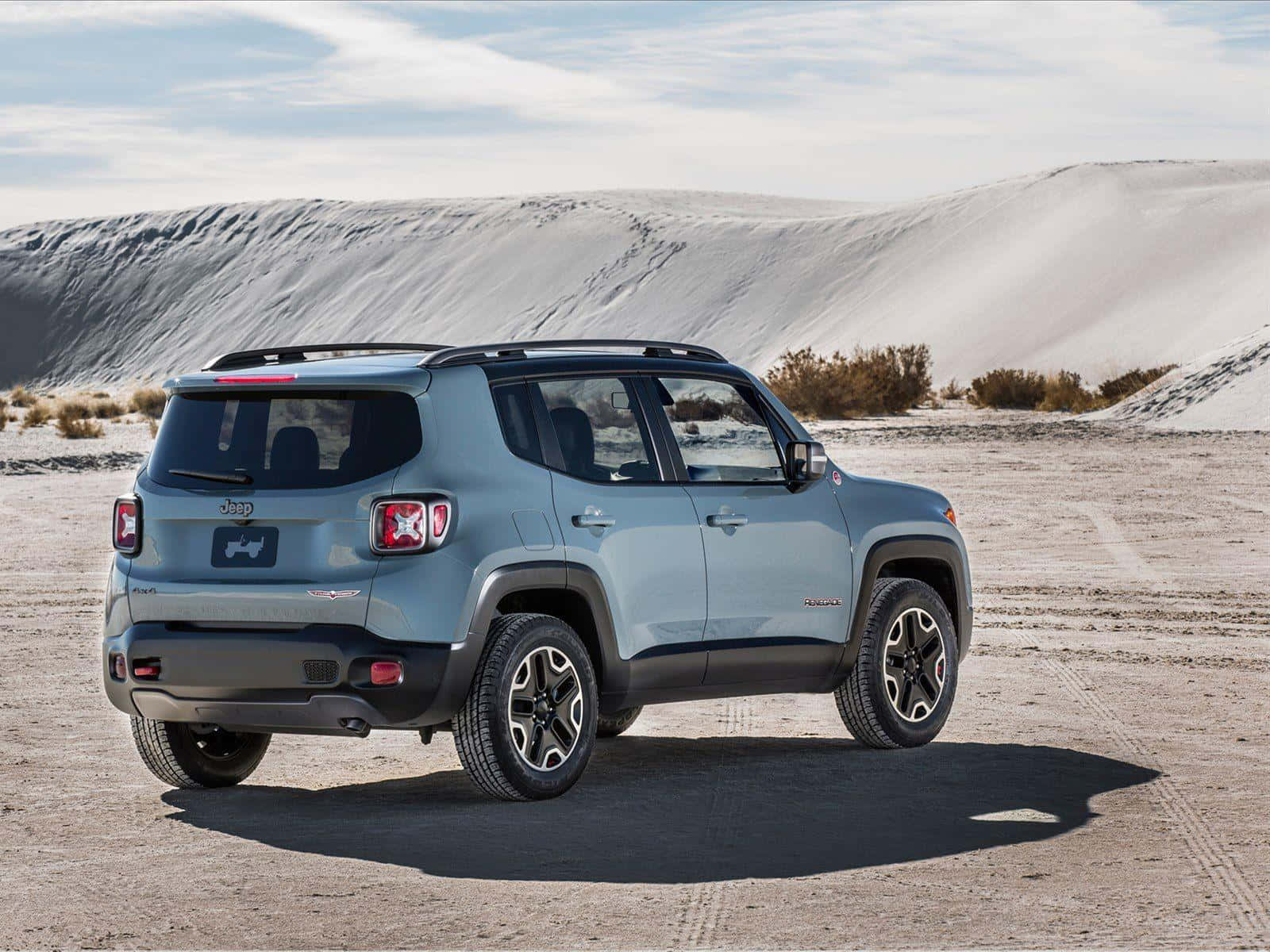 Jeep Renegade 桌布 壁紙 — 一輛淺藍色Jeep Renegade在陽光明媚的沙漠平原上，背景有起伏的沙丘和稀疏的灌木叢，天空明亮。