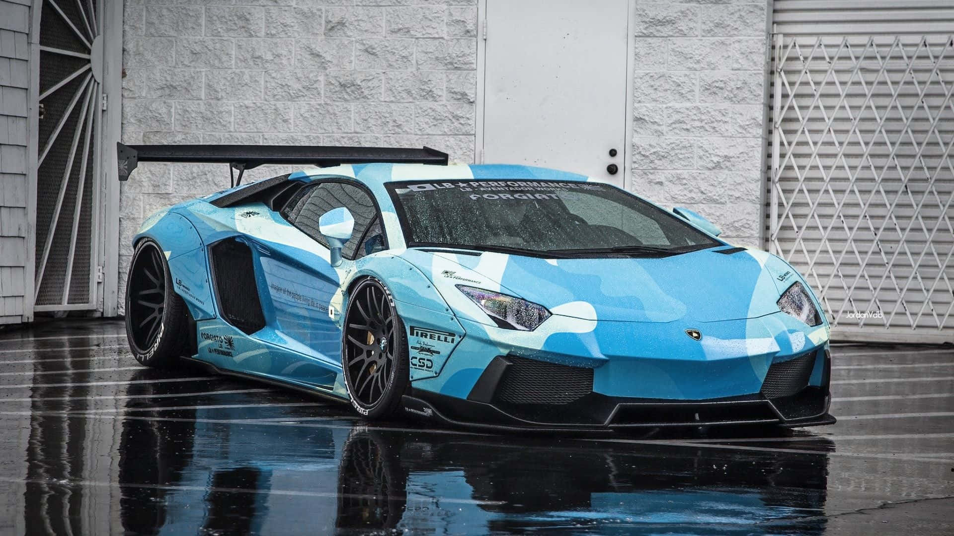 跑車 桌布 壁紙 — 一輛淺藍色和白色的藍寶堅尼 Aventador 帶有賽車貼紙，停在濕漉漉的柏油路面上，在灰色車庫門前映照出其流線型車身。