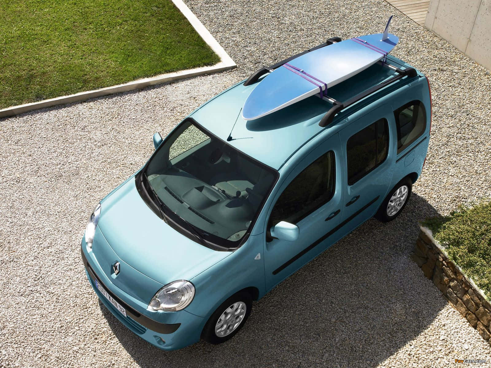 Renault Kangoo 桌布 壁紙 — 一輛淺藍色小型廂型車，車頂行李架上綁著一塊衝浪板，停在碎石車道上，旁邊是綠草。