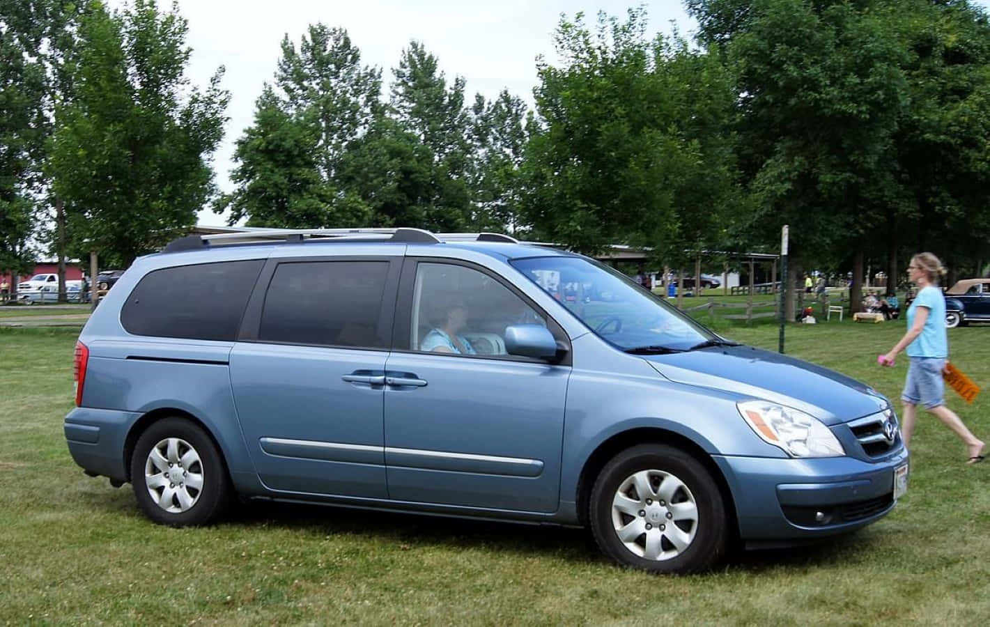 Hyundai Entourage 桌布 壁紙 — 一輛淺藍色小型貨車停在草地上，後面有樹木，附近有一個女孩在行走。