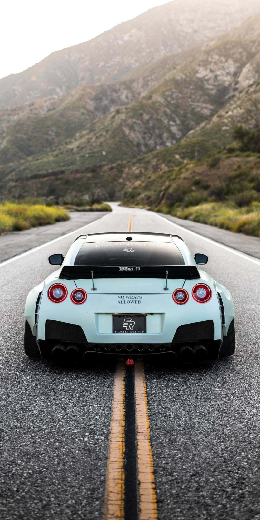 汽車 4K 桌布 壁紙 — 一輛淺藍色日產GT-R在朦朧天空下，沿著一條有黃色分隔線的蜿蜒山路飛馳而下。