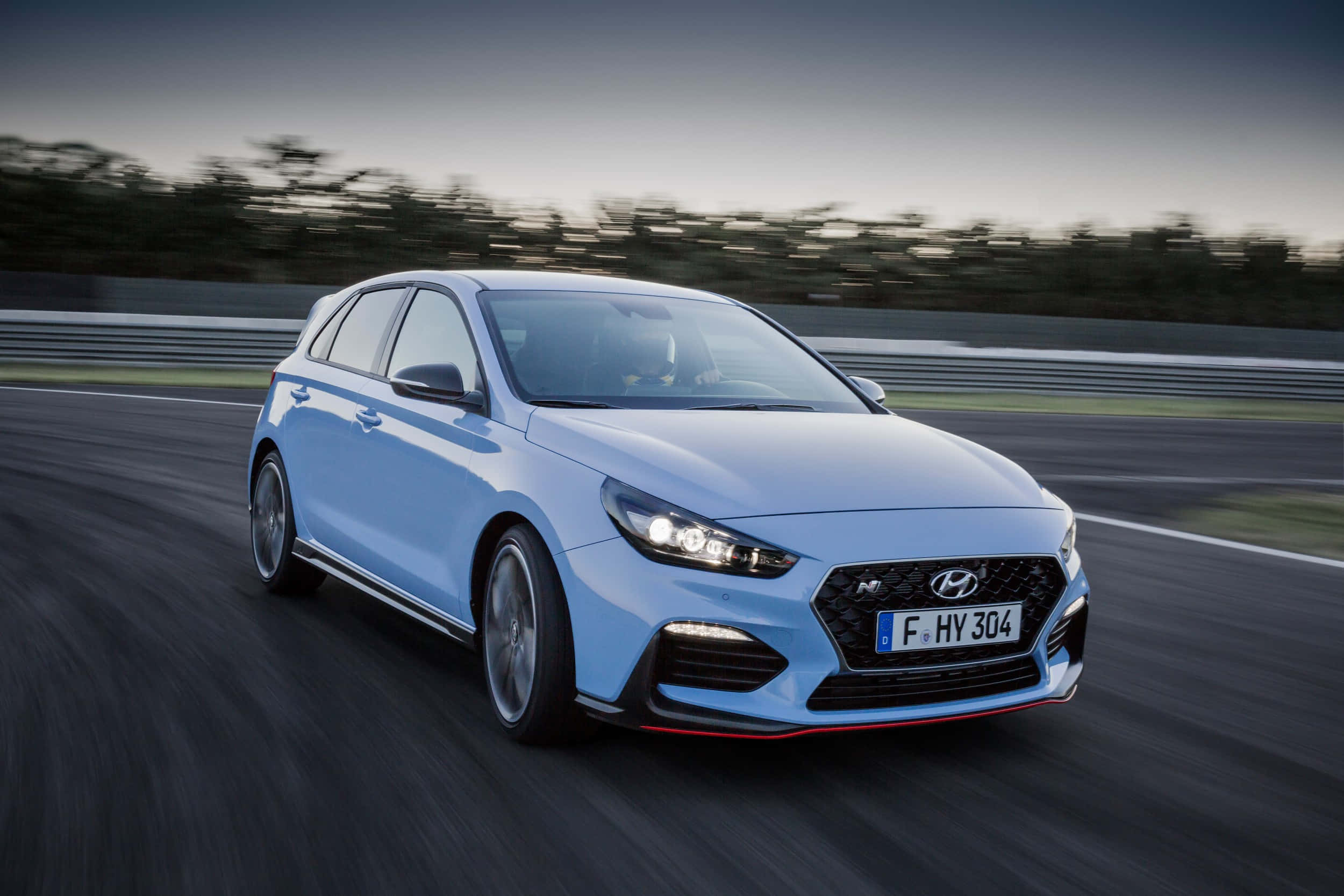 Hyundai 桌布 壁紙 — 一輛淺藍色現代 i30 N 掀背車在賽道上疾馳，帶有動態模糊和發光的頭燈。