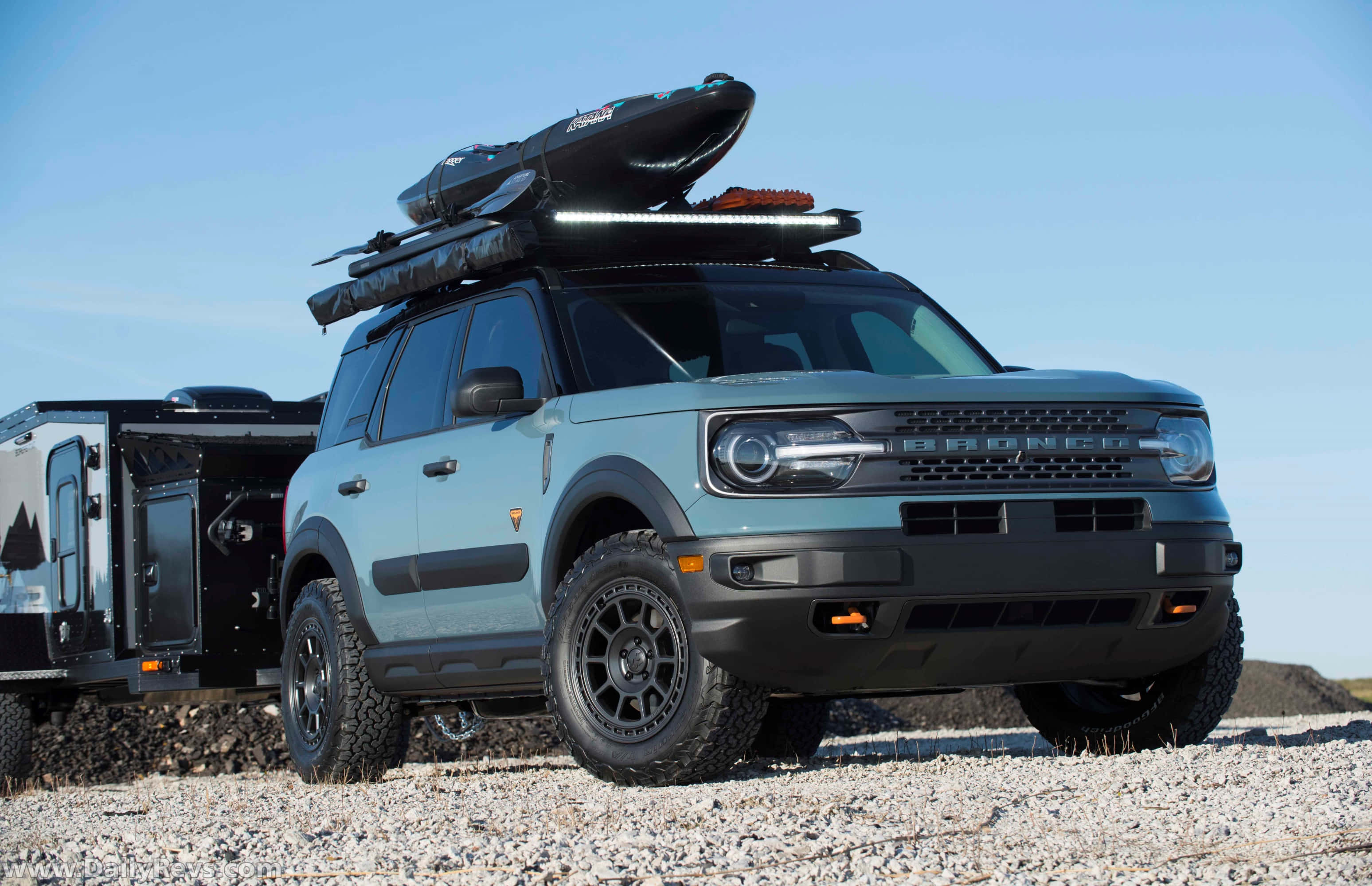 Ford Bronco 桌布 壁紙 — 一輛淺藍色的福特Bronco SUV車頂架上載著一艘皮划艇，在晴朗的藍天下，準備在碎石沙漠道路上展開冒險。