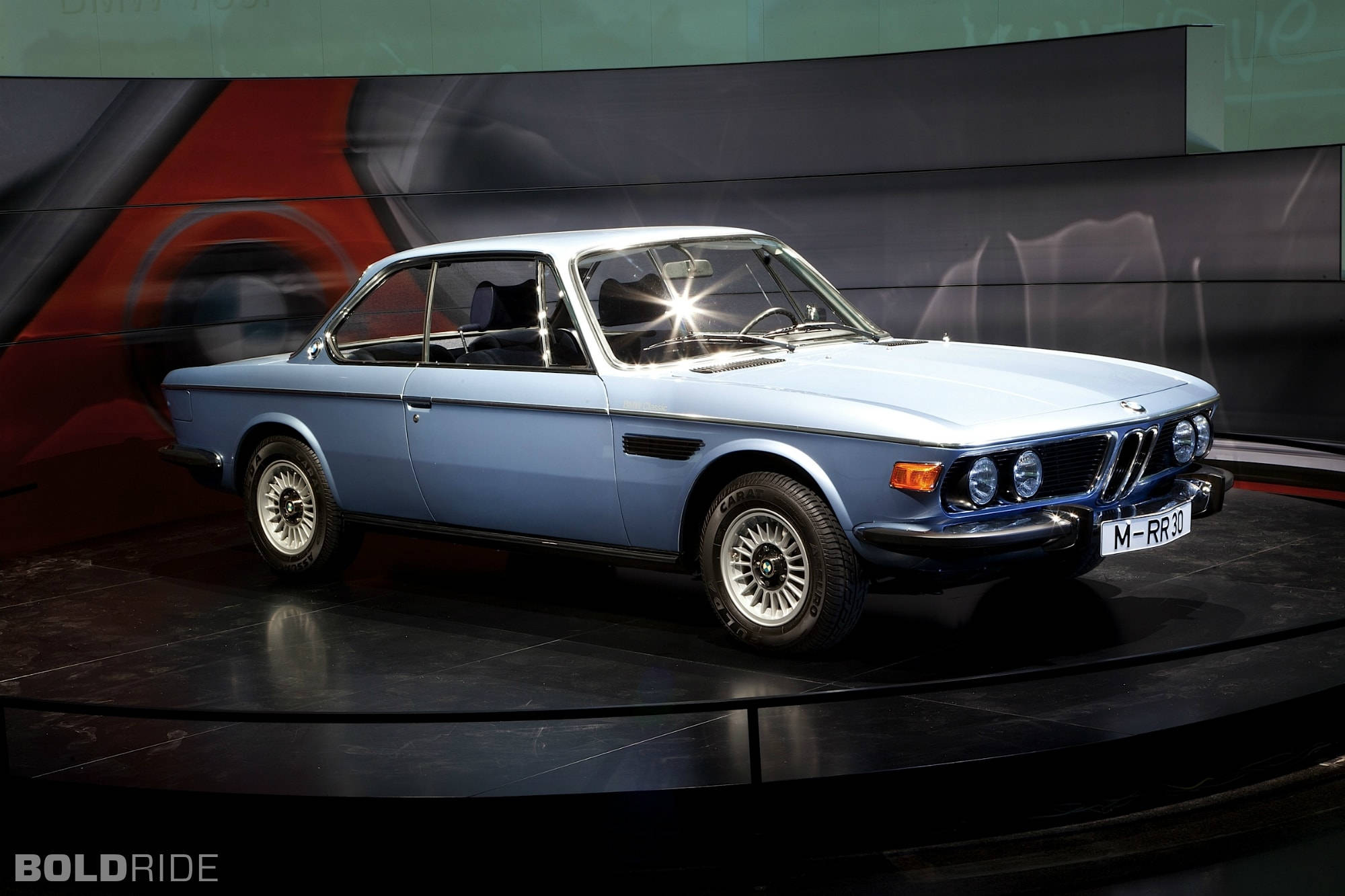 classic bmw 桌布 壁紙 — 一輛淺藍色經典BMW 2002 tii雙門跑車在深色旋轉展示台上於攝影棚燈光下閃閃發光。