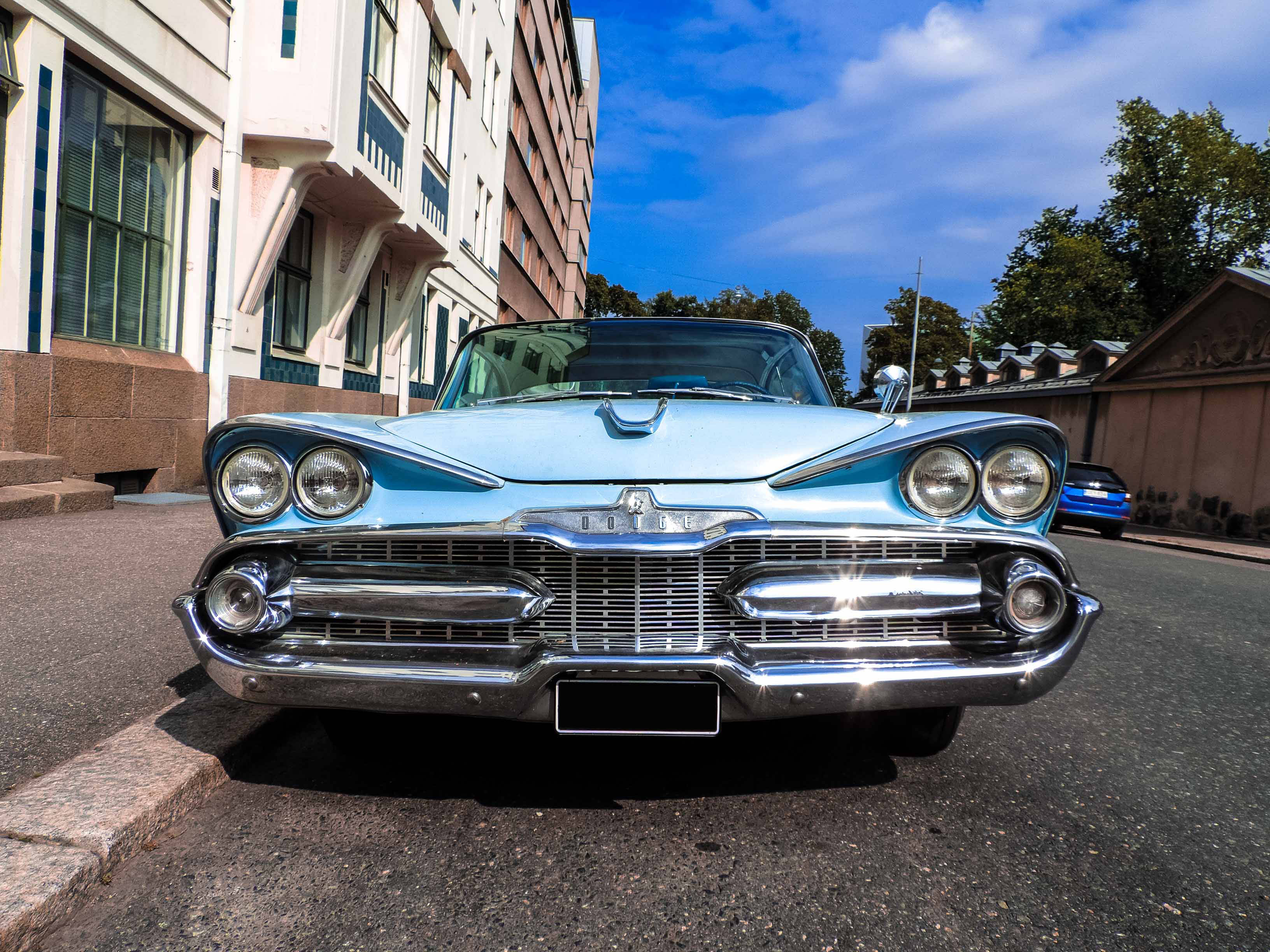 dodge iPhone 桌布 壁紙 — 一輛淺藍色經典汽車，帶有鍍鉻細節，停在城市街道上，天空湛藍。
