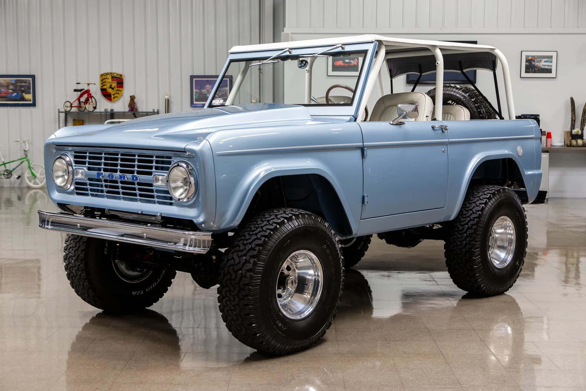 Ford Bronco 桌布 壁紙 — 一輛淺藍色經典福特Bronco，配備鍍鉻飾件和超大輪胎，自豪地停放在乾淨、光線充足的車庫中。