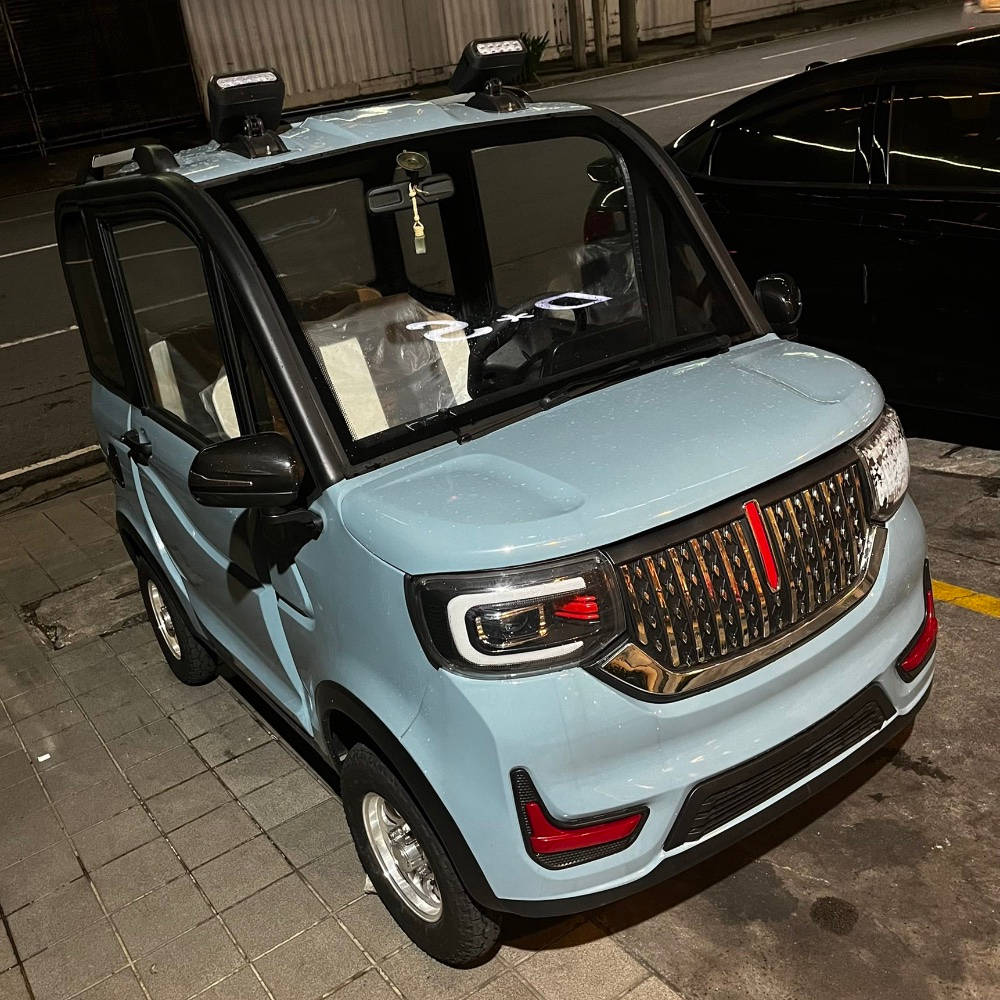 淺藍色 桌布 壁紙 — 一輛淺藍色緊湊型電動車停在夜間鋪砌的街道上，帶有發光的車頭燈和紅色飾邊。