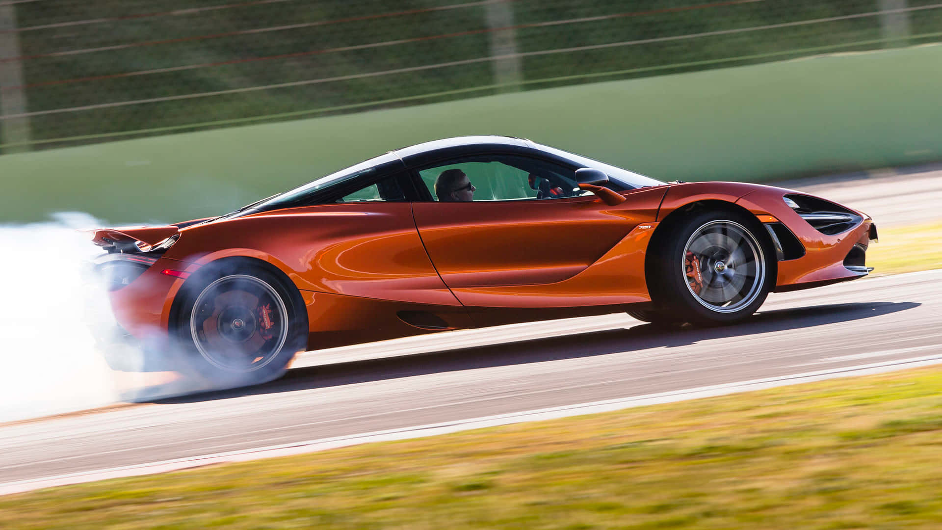 Race Track 桌布 壁紙 — 一輛火橙色的McLaren跑車在賽道上甩尾，後輪冒出滾滾濃煙。