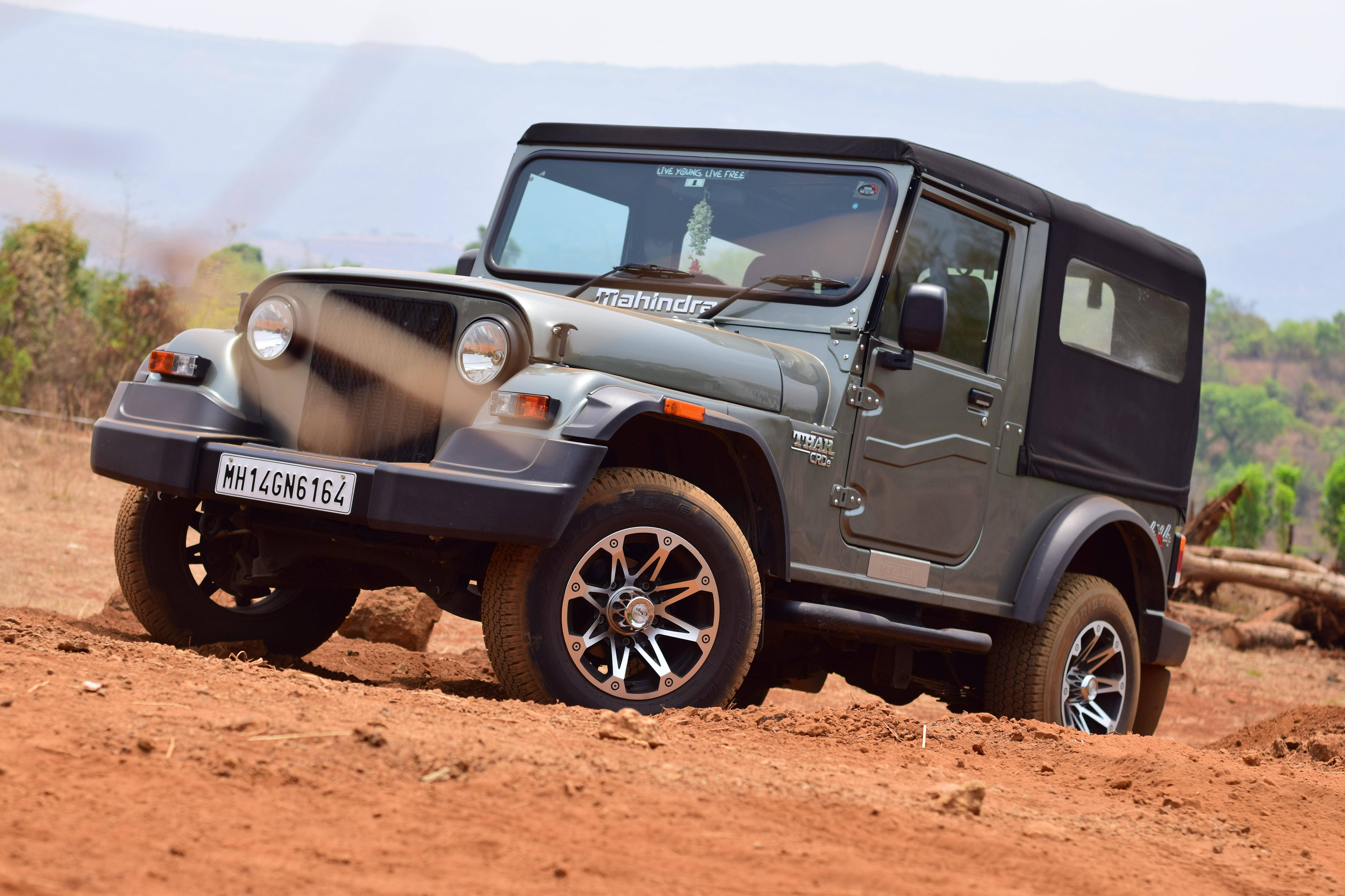 電腦 桌布 壁紙 — 一輛灰色Mahindra Thar SUV在晴朗天空下，於紅色泥土路面上行駛，揚起塵土，遠處有山丘。