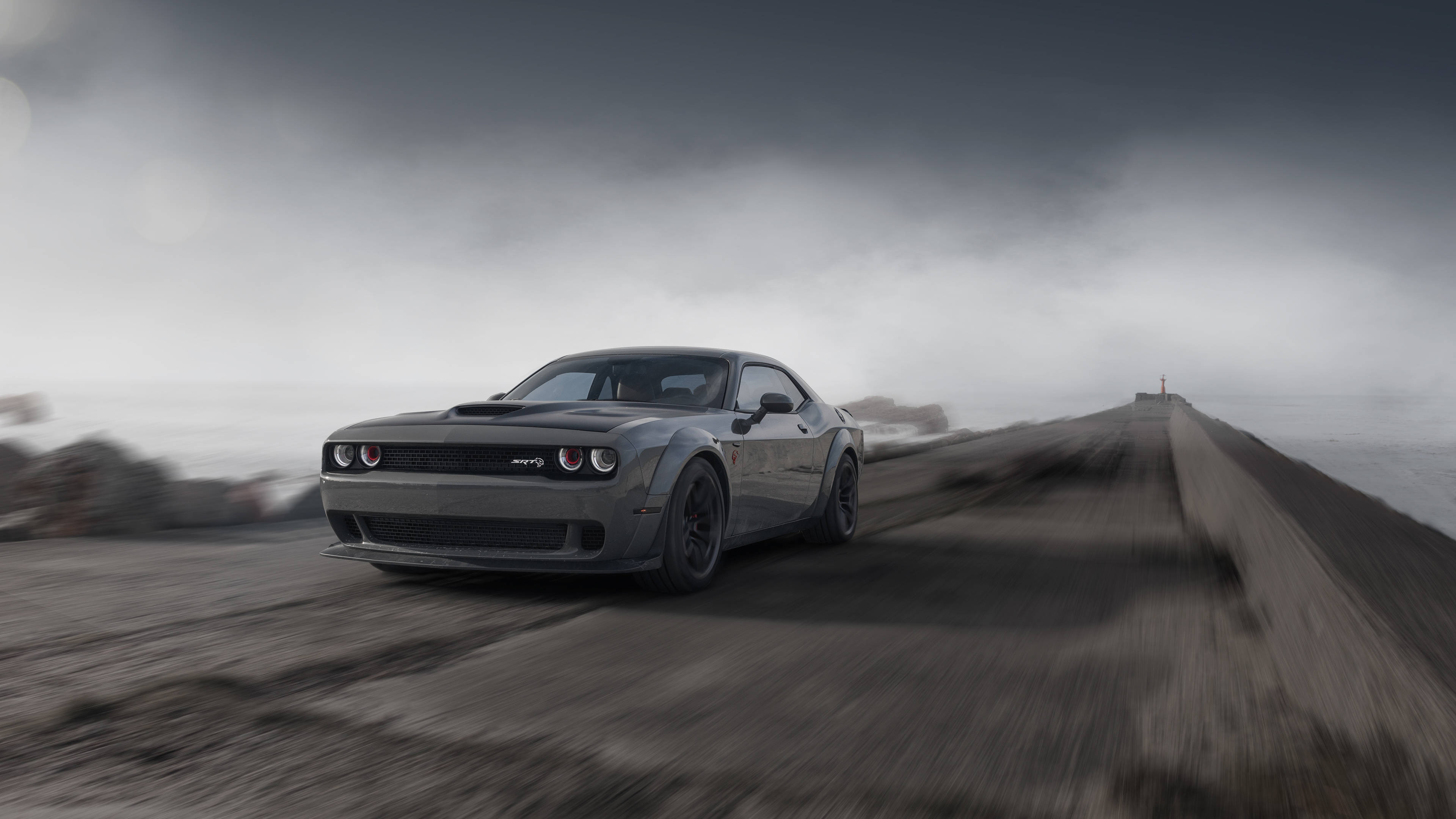Dodge 桌布 壁紙 — 一輛灰色的 Dodge Challenger Hellcat 在陰暗的天空下，沿著霧氣瀰漫的海岸公路疾馳。