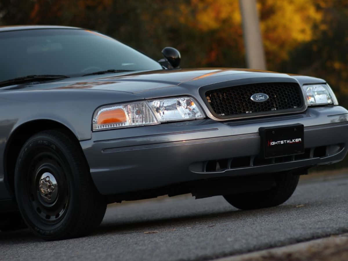 Ford Crown Victoria 桌布 壁紙 — 一輛灰色福特皇冠維多利亞警車停在柏油路上，身後秋樹在溫暖光線中閃耀。