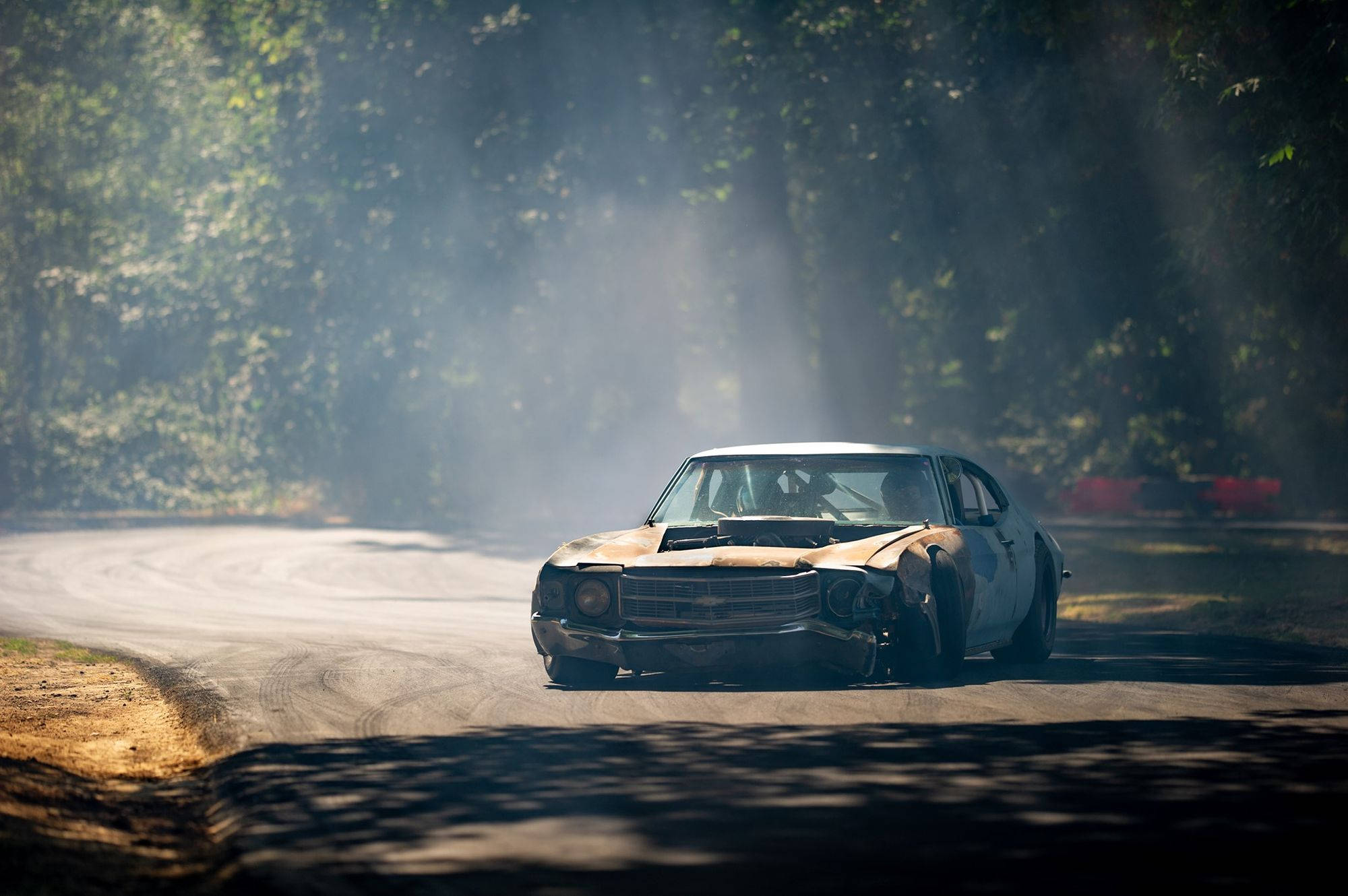 drifting 桌布 壁紙 — 一輛生鏽的復古肌肉車在樹林彎道中飄移，揚起灰塵和煙霧，陽光斑駁。