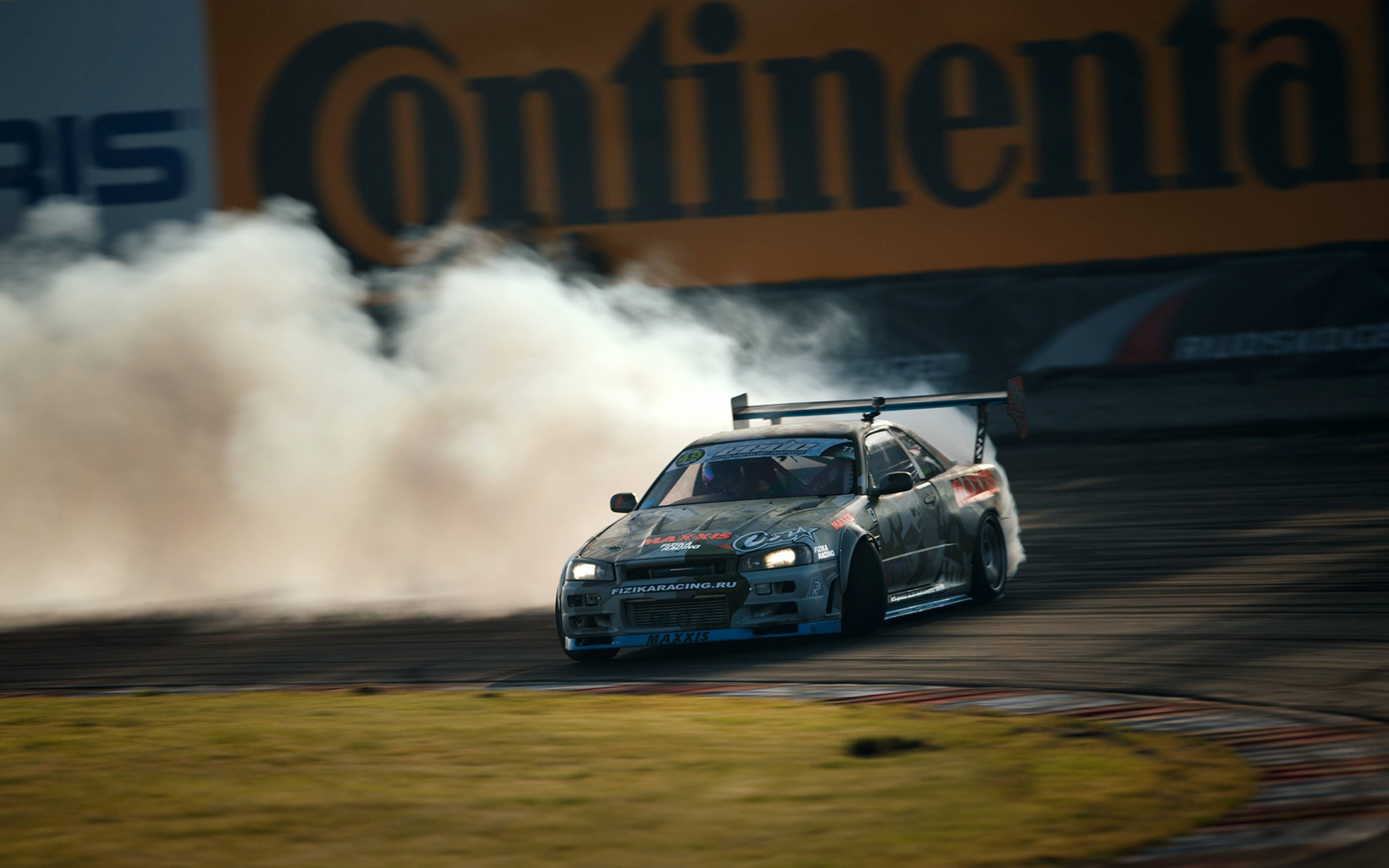drifting 桌布 壁紙 — 一輛甩尾賽車在明亮燈光下於賽道彎角滑行，揚起濃煙。