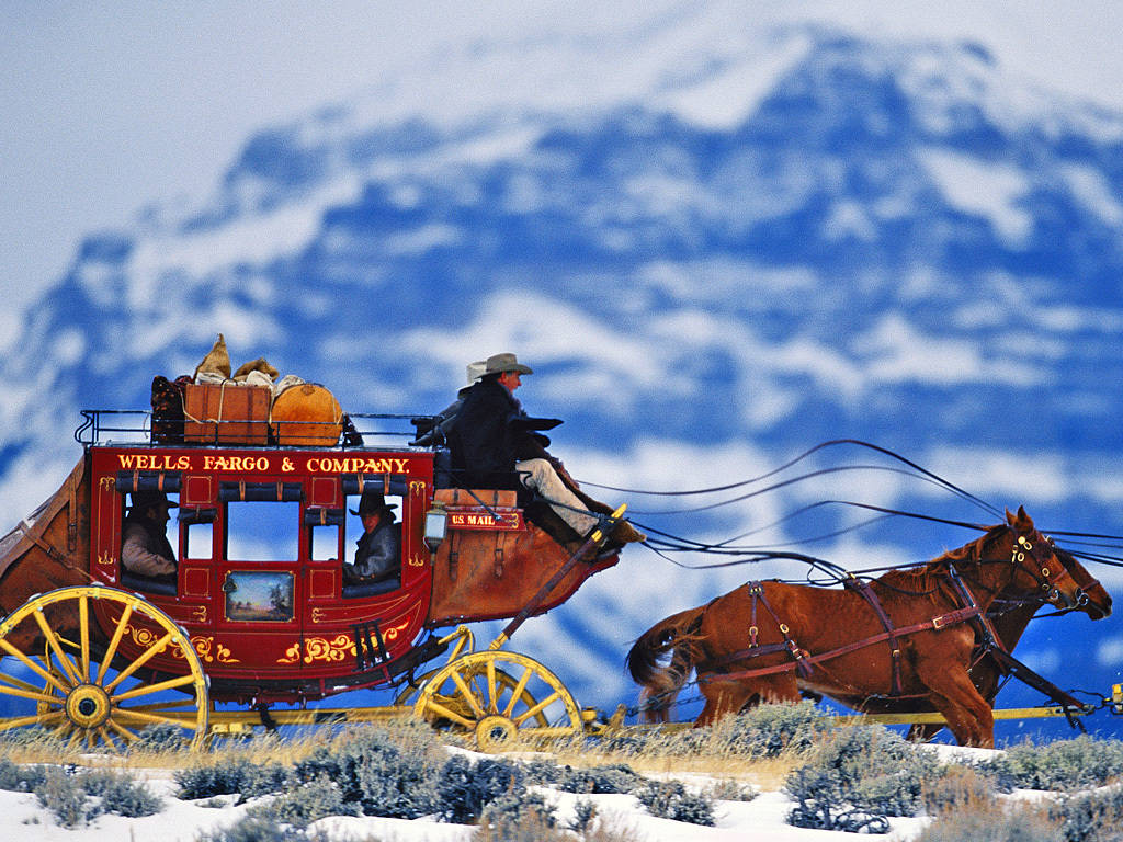  壁紙 — 一輛由兩匹棕色馬匹拉動的紅色 Wells Fargo 驛馬車，正穿越白雪覆蓋的山口，背景是白雪皚皚的山峰。
