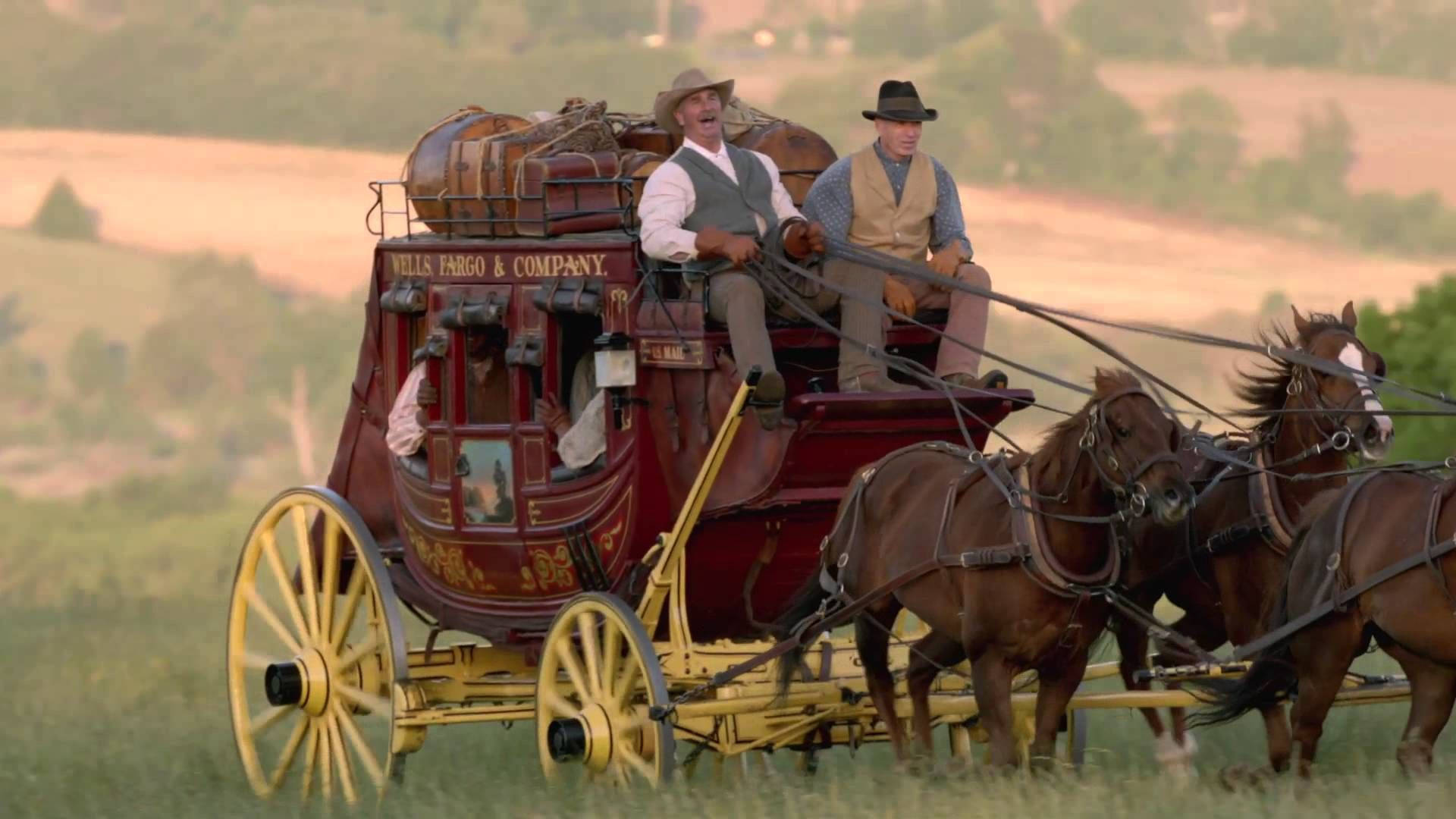 transportation 桌布 壁紙 — 一輛由兩匹馬拉動的 Wells Fargo 驛馬車，載著穿著時代服裝的騎手，在草地上疾馳。