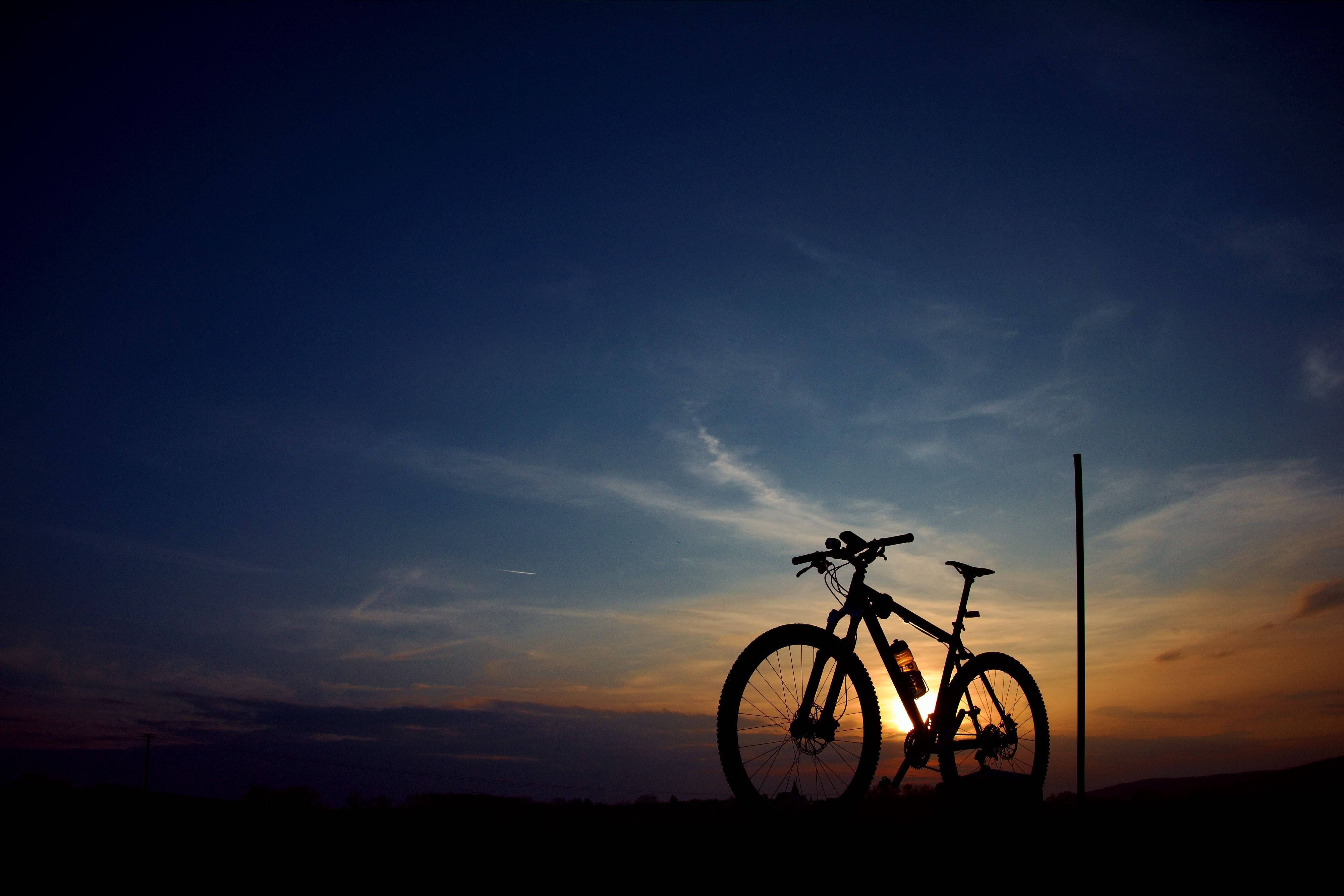 Mountain Bike 桌布 壁紙 — 一輛登山車的剪影，映襯著充滿活力的暮色天空，帶有橙色和深藍色的雲彩條紋。