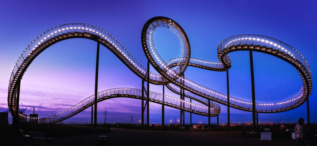 Roller Coaster 桌布 壁紙 — 一輛發光的雲霄飛車在紫色和藍色色調的暮色天空中蜿蜒前行。
