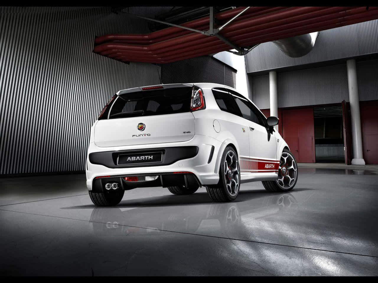 Abarth 桌布 壁紙 — 一輛白色 Abarth Punto EVO 跑車從後方四分之三角度展示在現代工業車庫內，帶有紅色點綴和拋光混凝土地板。