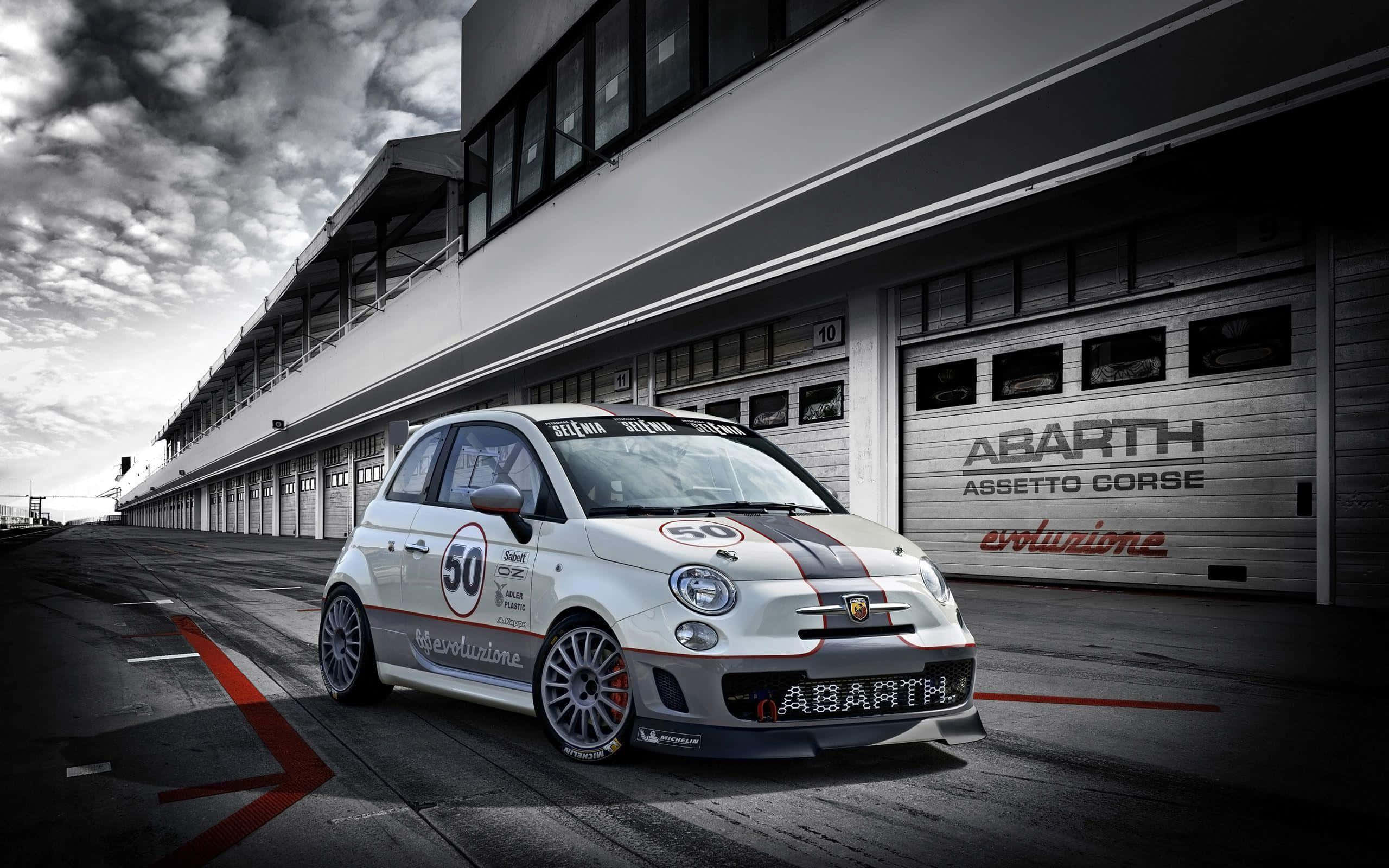 Abarth 桌布 壁紙 — 一輛白色 Abarth 賽車，車號 50，停放在賽車場車庫前，背景是戲劇性的多雲天空。