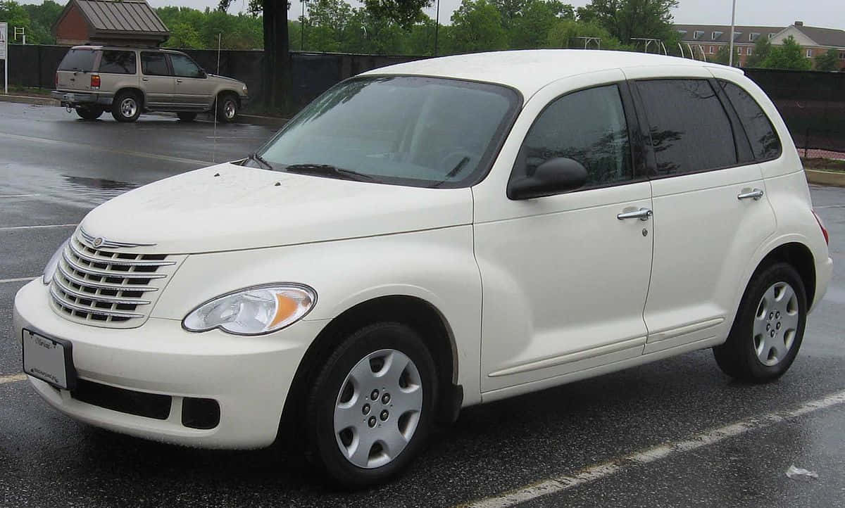 Chrysler Pt Cruiser 桌布 壁紙 — 一輛白色 Chrysler PT Cruiser 停放在濕漉漉的瀝青停車場，背景有樹木和圍欄。