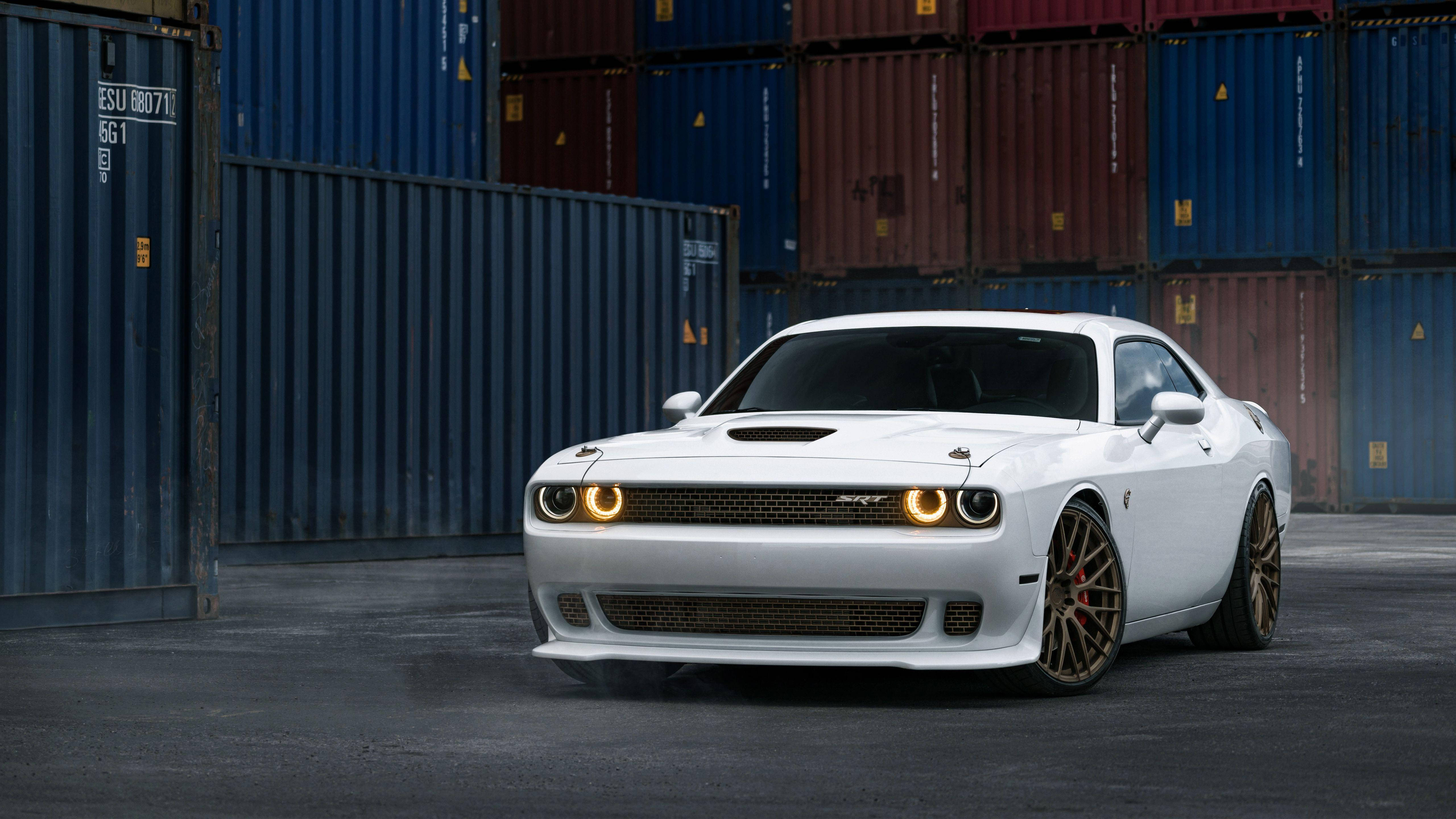 跑車 桌布 壁紙 — 一輛白色 Dodge Challenger SRT Hellcat 亮著車頭燈，大膽地停在堆疊的藍色和紅色貨櫃前。