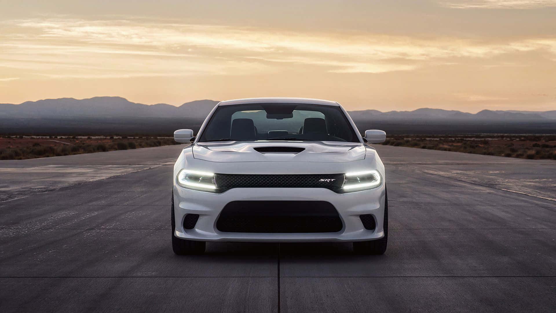 Dodge Charger 桌布 壁紙 — 一輛白色 Dodge Challenger SRT 在沙漠公路上向前行駛，背景是日落和山脈。