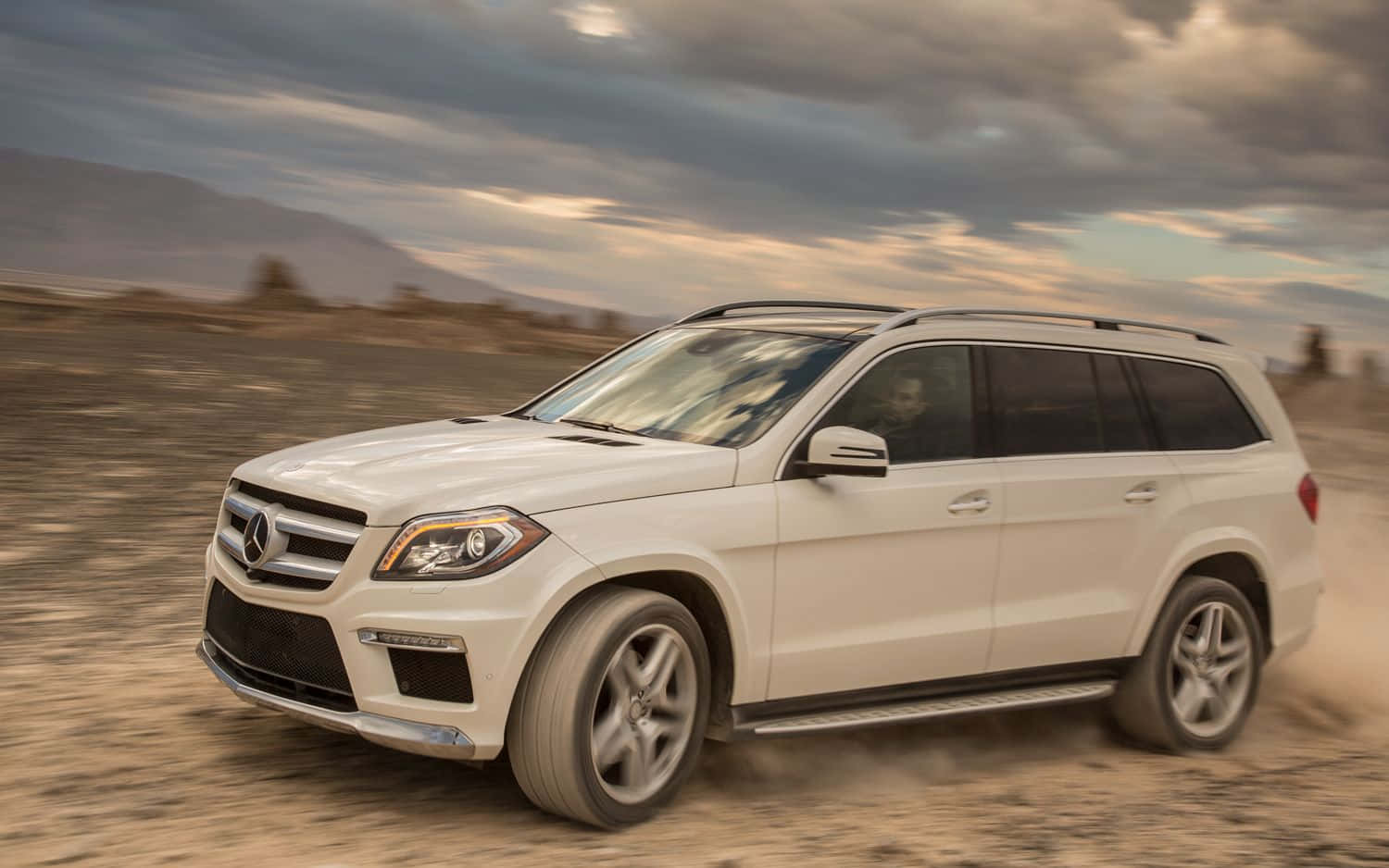 Mercedes-benz Gl-class 桌布 壁紙 — 一輛白色 Mercedes GLS SUV 在戲劇性的多雲天空下，疾馳過塵土飛揚的沙漠景觀。