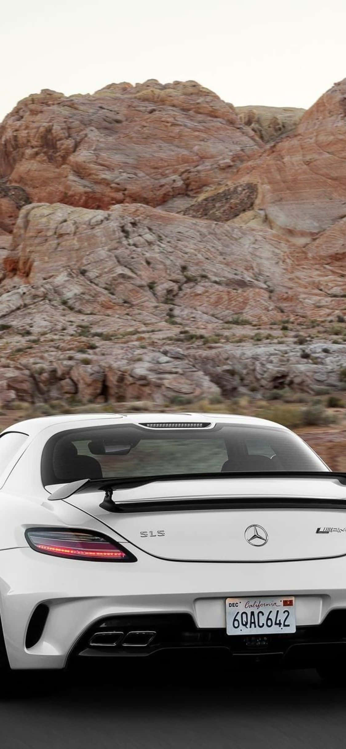 Mercedes 桌布 壁紙 — 一輛白色 Mercedes SLS AMG 跑車在朦朧天空下，駛過有紅色岩層的沙漠峽谷。